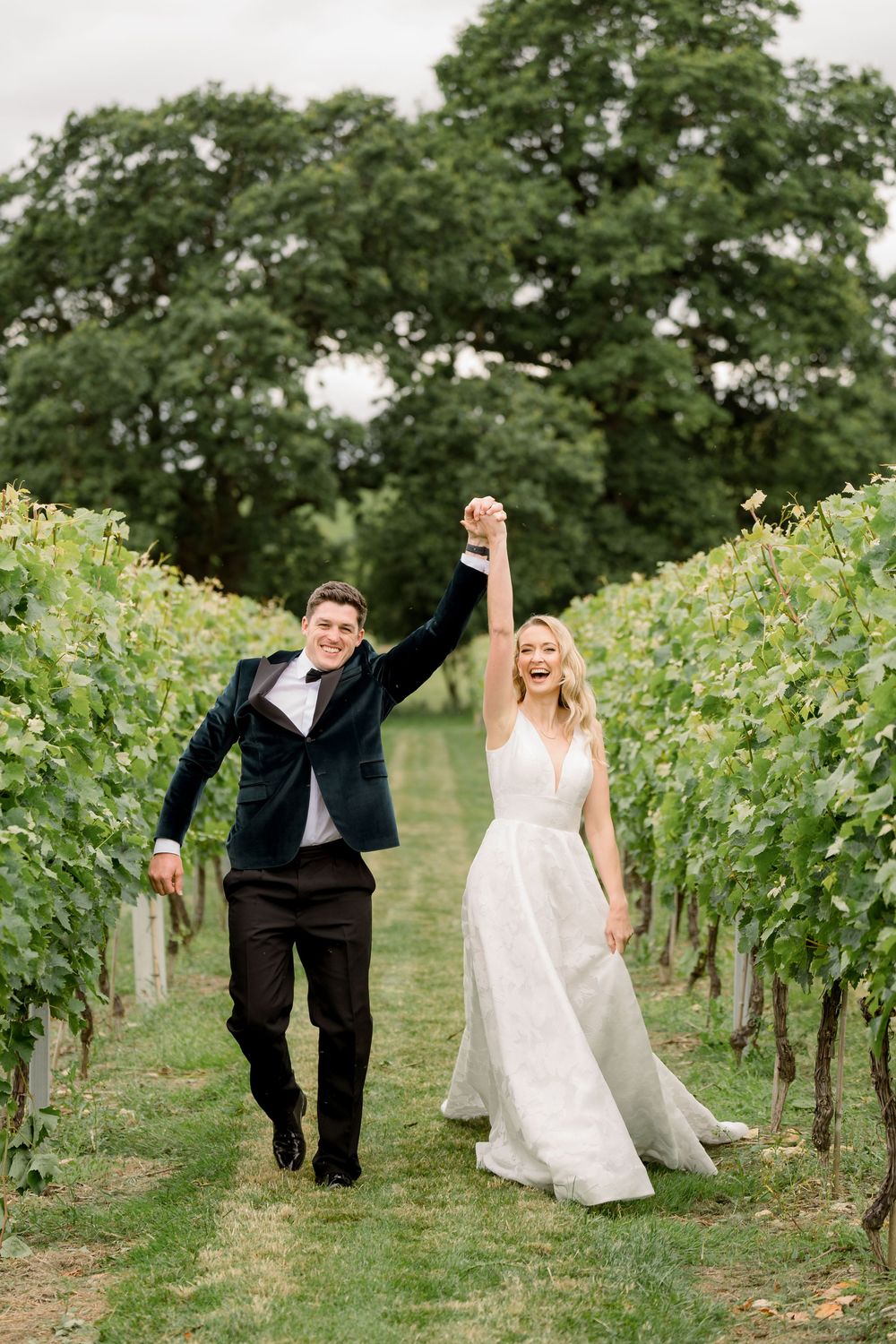 A couple playfully poses among rows of grapevines in a vineyard on their wedding day.