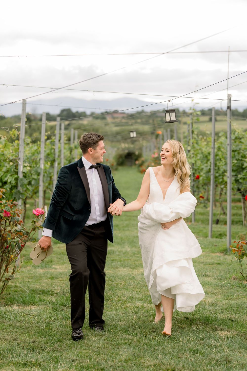 A couple in wedding attire playfully runs through a vineyard on their special day.