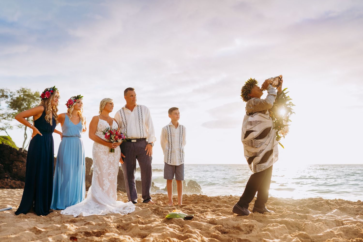 A group gathers on a scenic beach at sunset during a romantic coastal celebration with soft golden light. A Maui beach elopement with family