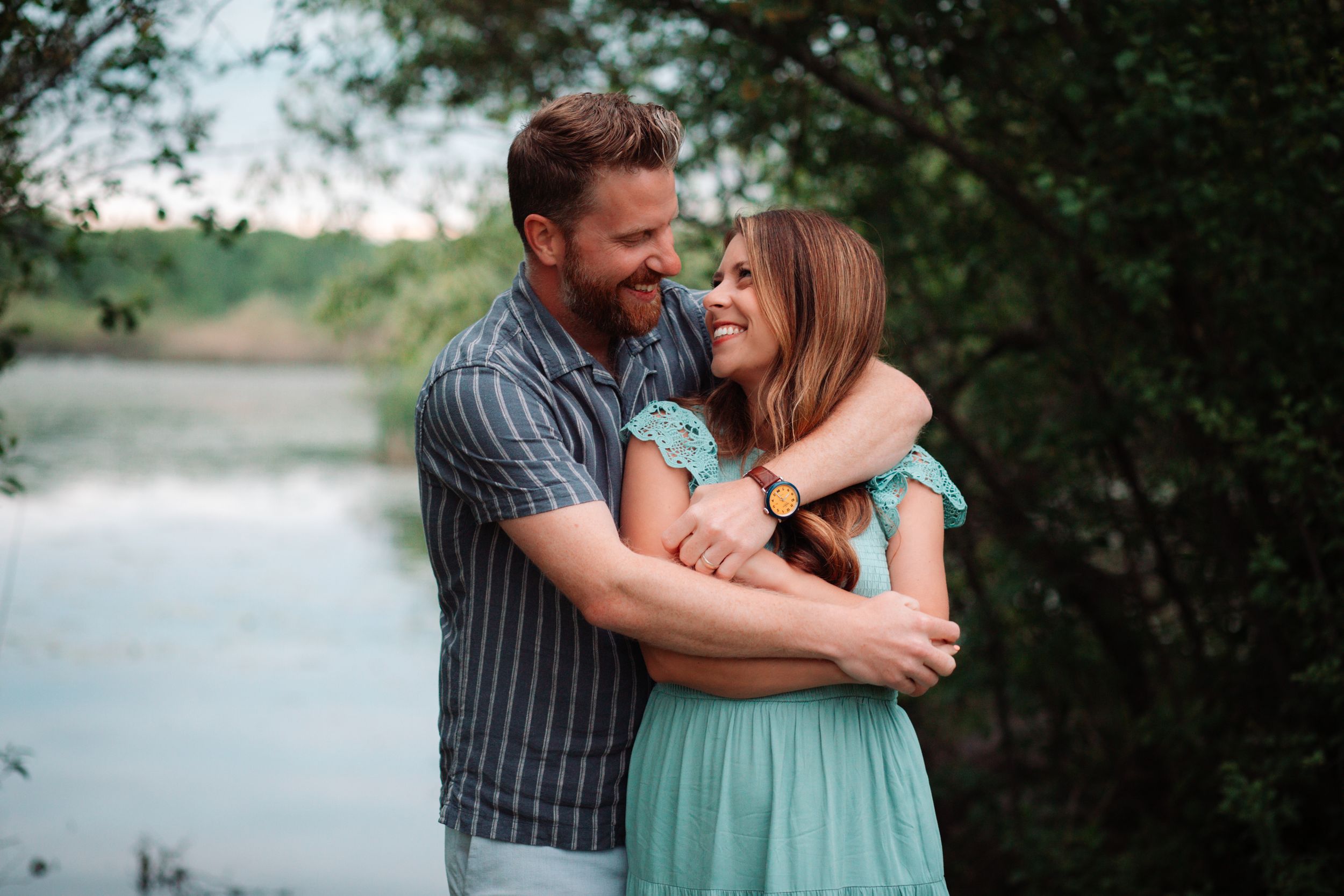 A couple embraces by the water's edge during golden hour.