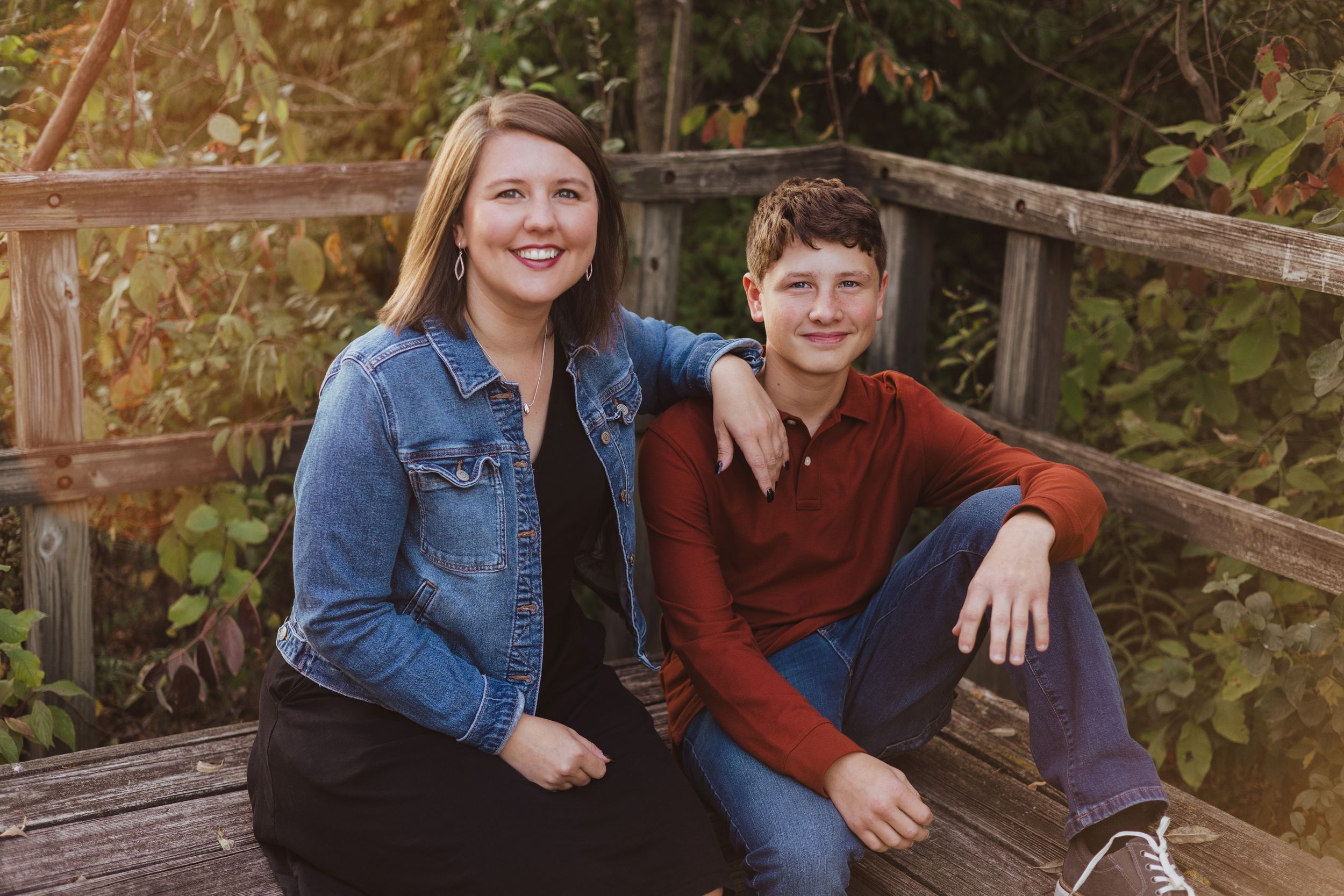 Two people sit together on a wooden bridge in casual outdoor attire.