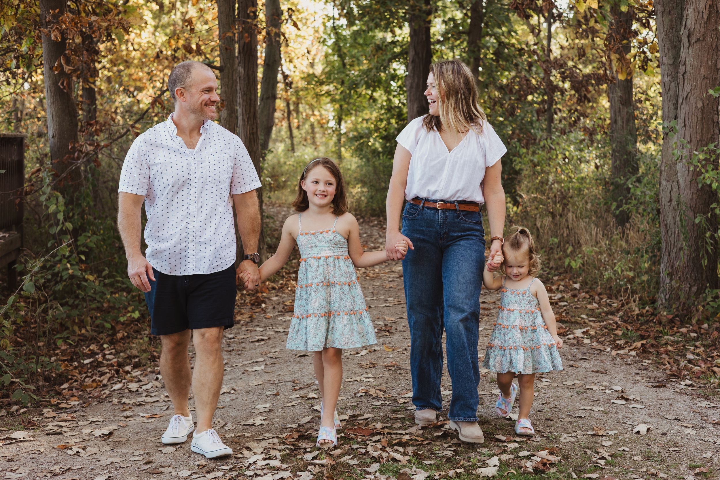 A family of four walks together on a wooded trail during autumn.