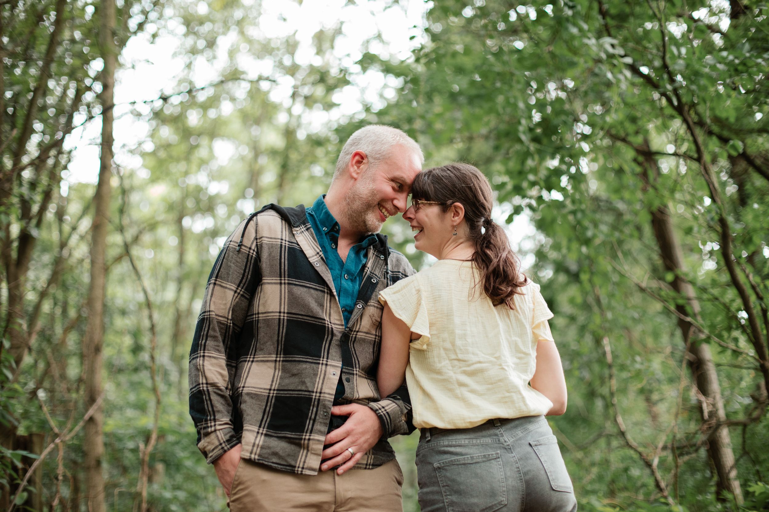 A couple shares an intimate moment together in a wooded setting.