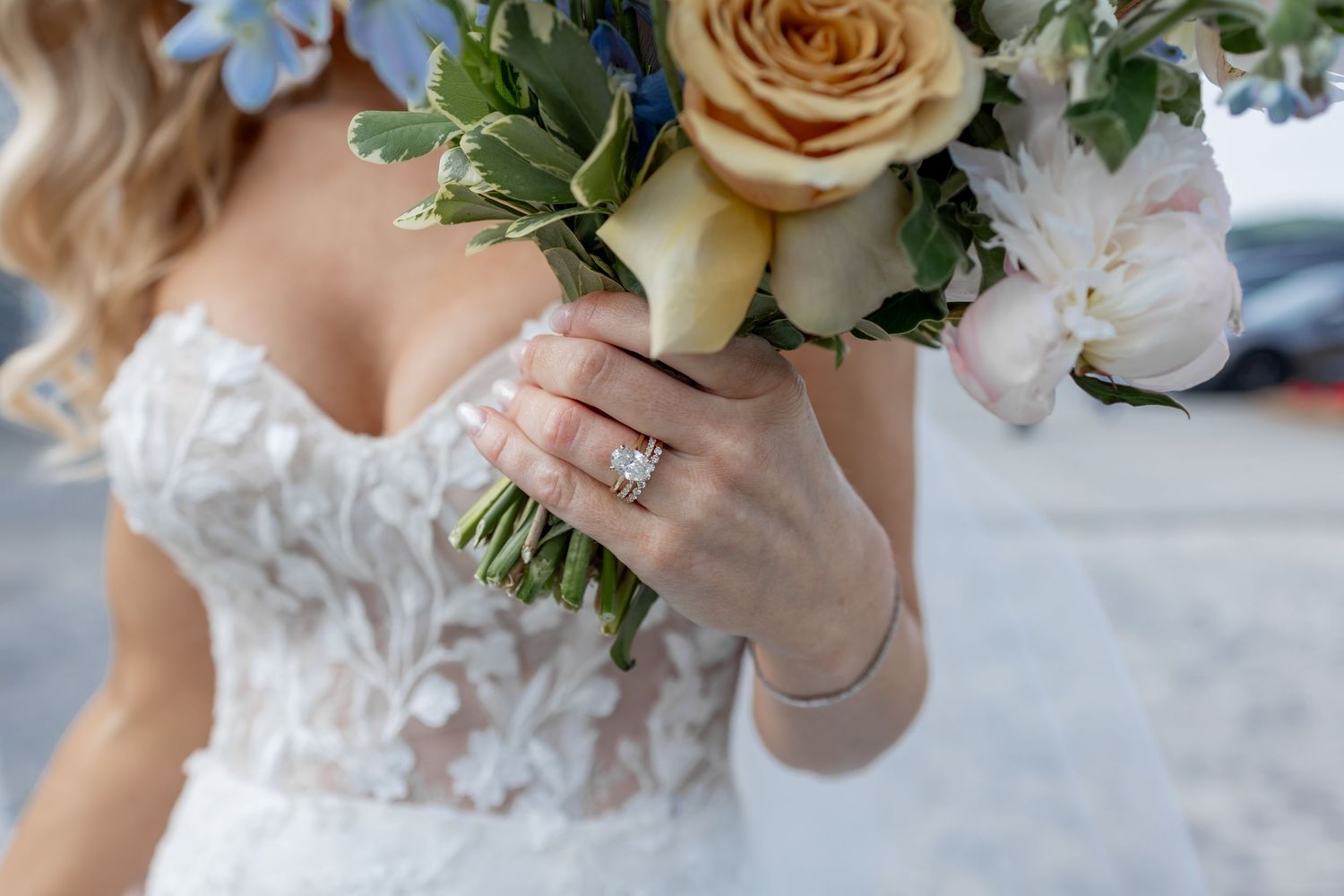 Elegant wedding bouquet with peach roses and white flowers held against a lace dress in natural lighting.