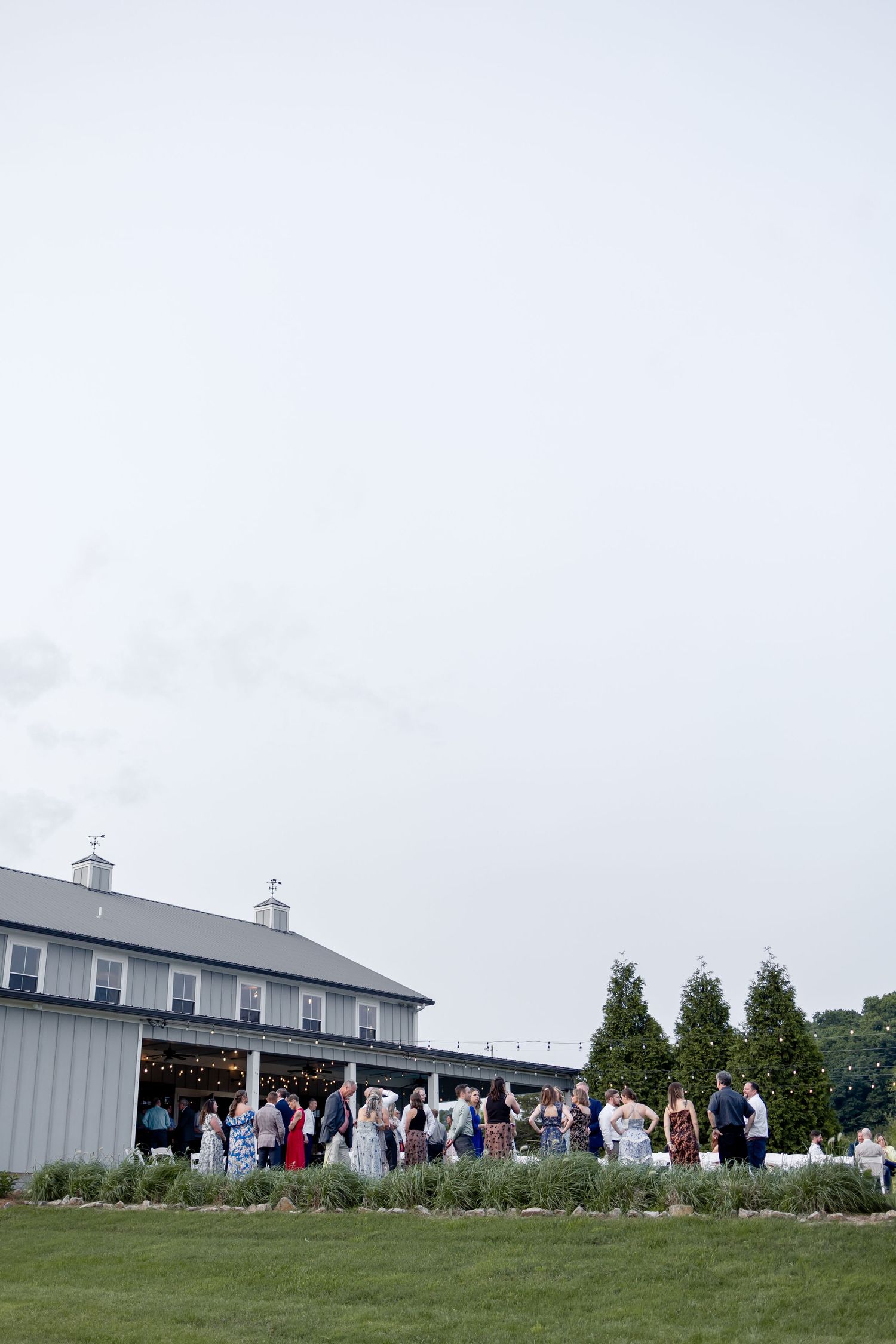 A large group of people gathered outside a white barn-style building for a special event on a grassy lawn.