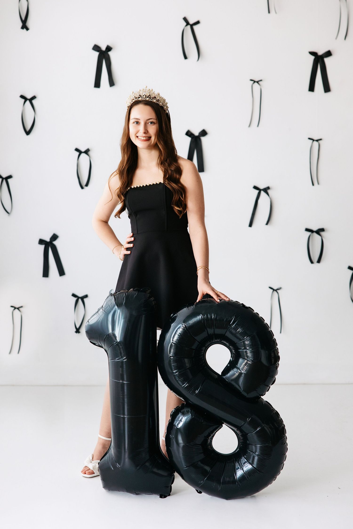 A black and white themed 18th birthday photo session with black balloons and decorative bows on the wall.