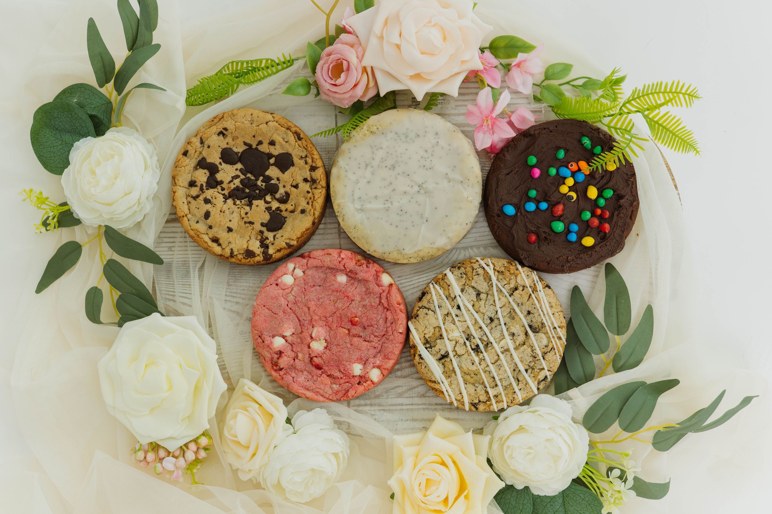 Gourmet cookies displayed with fresh roses and greenery on a light wooden surface.
