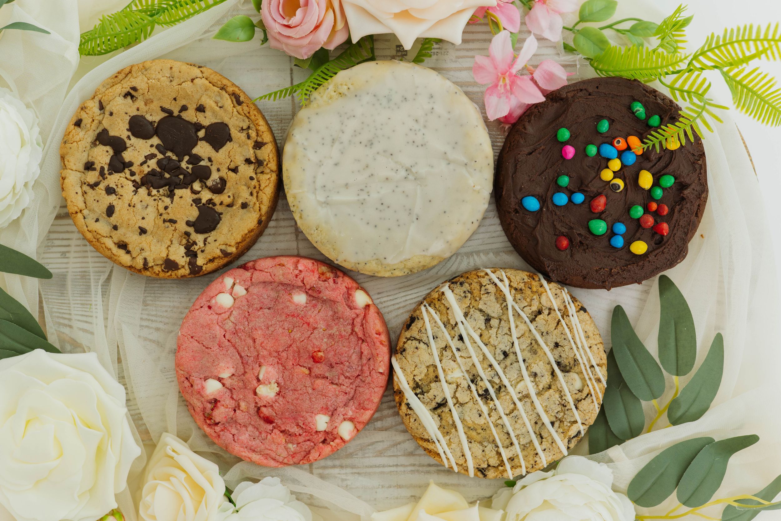 Various decorated cookies including chocolate, sugar, and pink varieties arranged with floral accents.