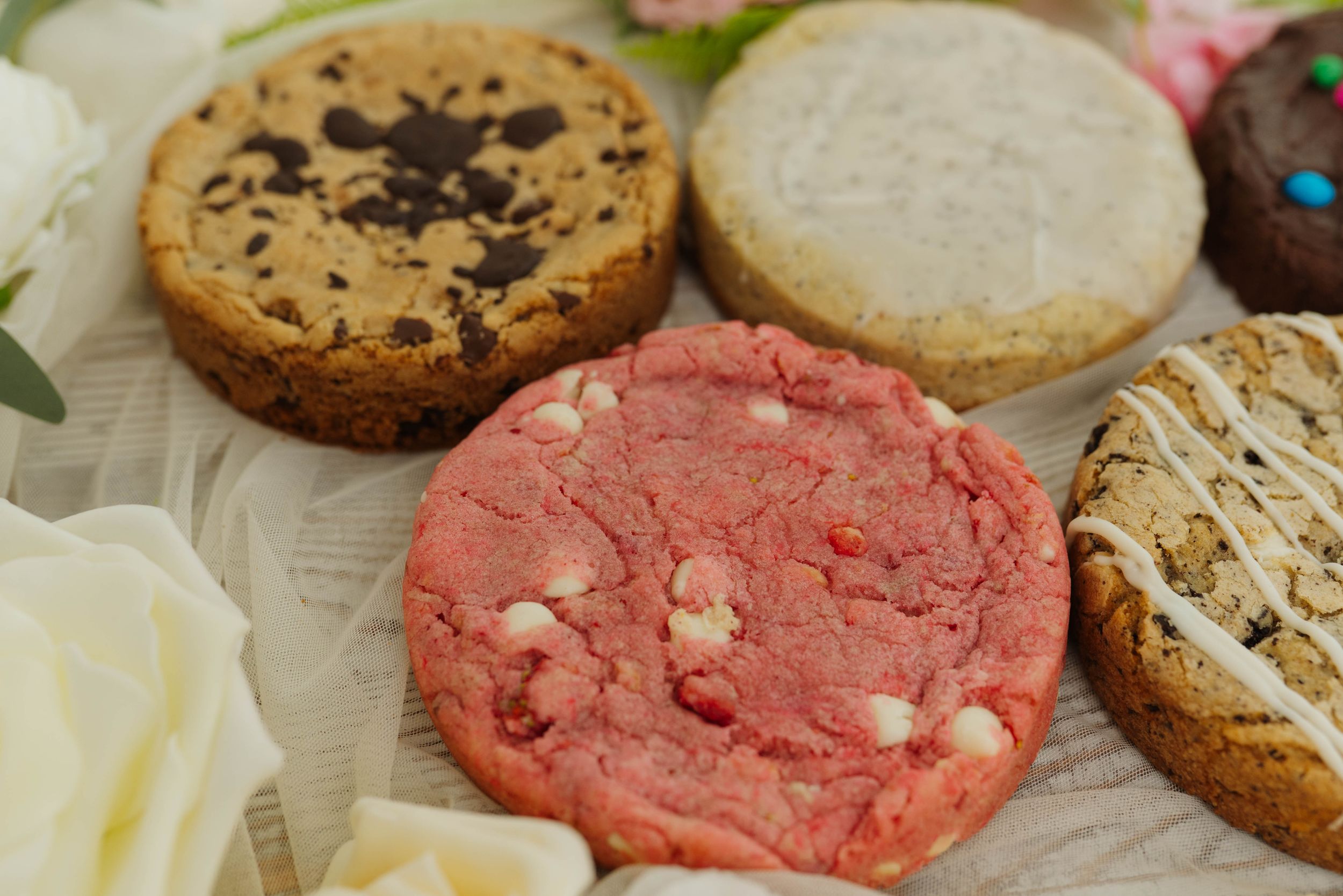 Assorted cookies with chocolate chips and pink frosting arranged with floral decorations.