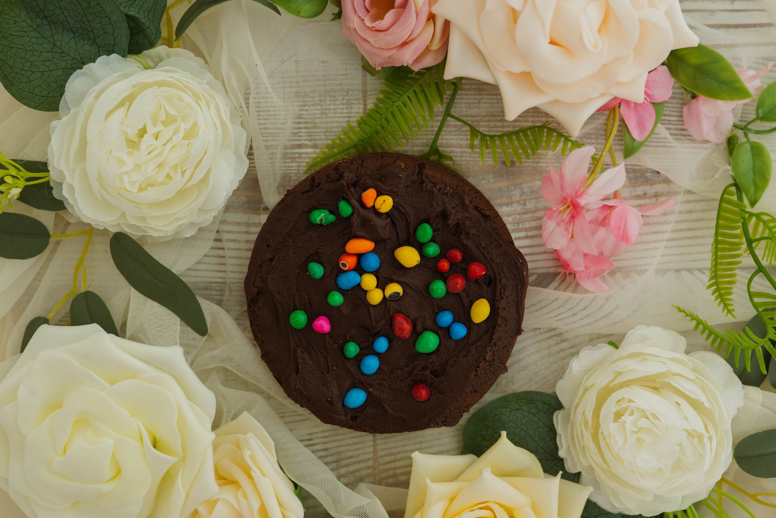 Chocolate cookies with rainbow sprinkles arranged among white and pink roses.