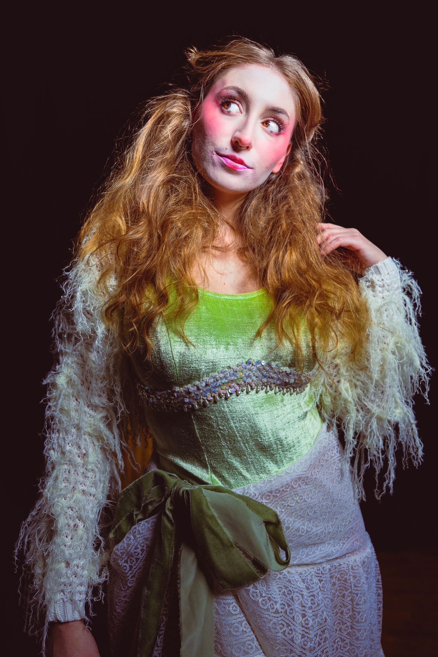A whimsical portrait featuring bright pink makeup, long wavy hair, and a green dress with a fluffy white shawl.