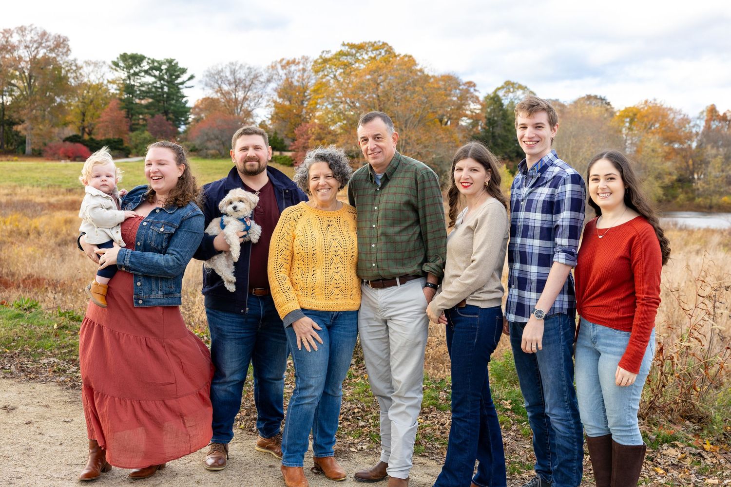 An extended family laughing and embracing together outdoors during autumn with colorful fall foliage in the background during family photos.