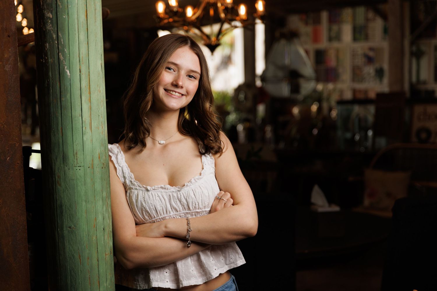 High school senior girl in white top leaning against a green pillar.