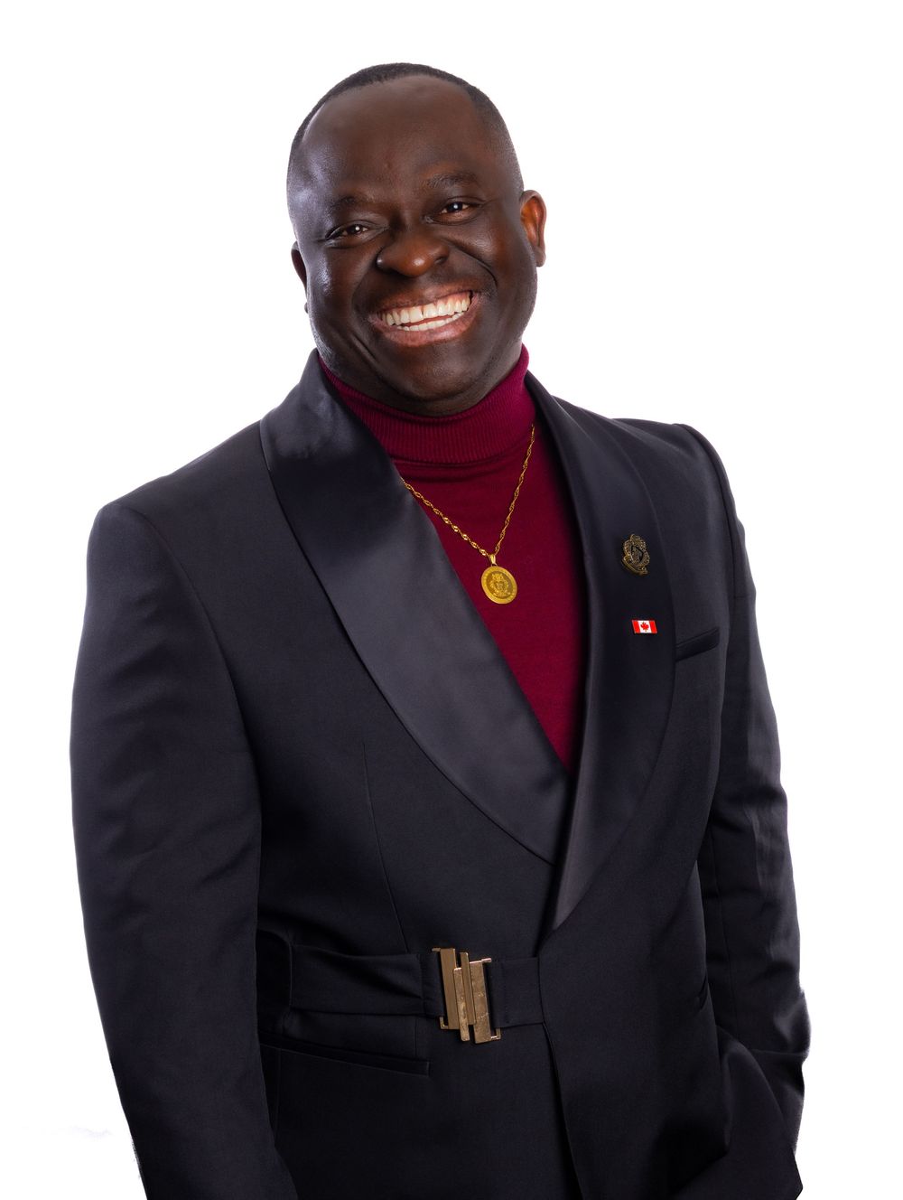 A person wearing a black suit and red turtleneck smiles warmly while posing for a professional portrait.