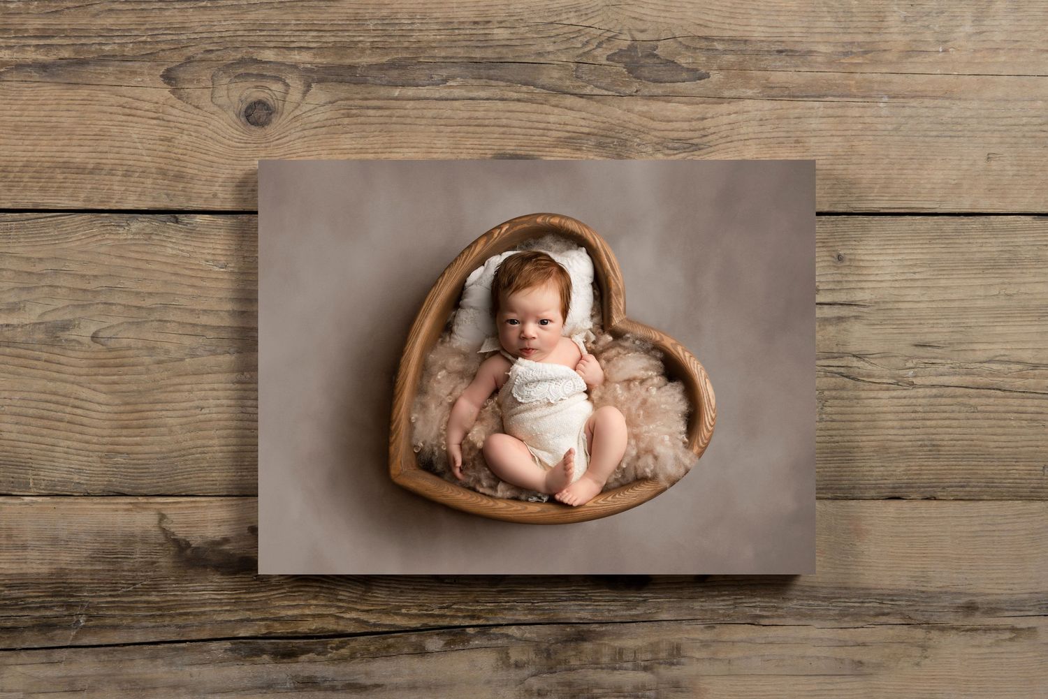 Newborn baby lying in heart-shaped wooden bowl on rustic wooden background.