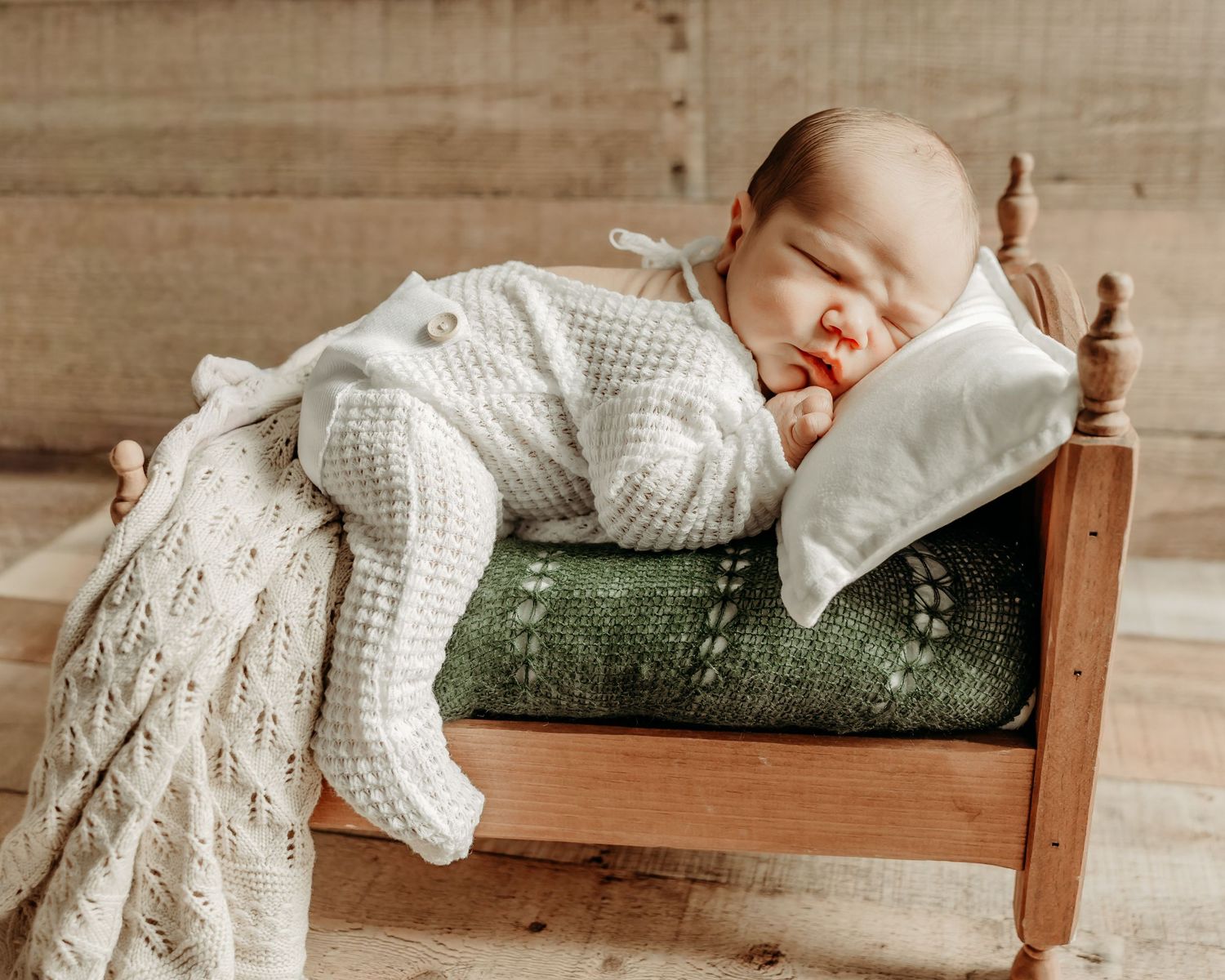 Sleeping newborn baby in white clothing lies peacefully on soft white bedding.