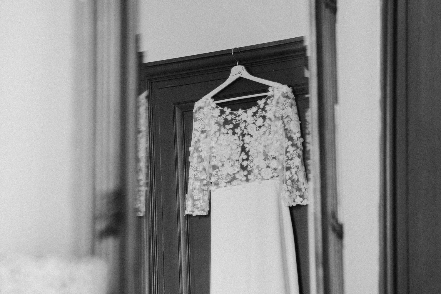 Black and white photo of floral lace wedding dress with long sleeves hanging on wooden door hanger.