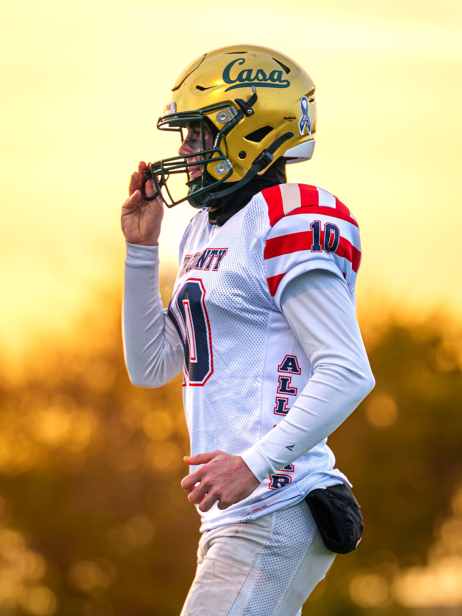 Football player in white jersey throwing a pass against an orange sunset sky during a game.