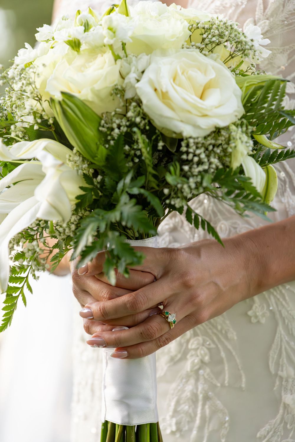 Close-up of elegant white wedding bouquet with roses and delicate greenery wrapped in white ribbon.