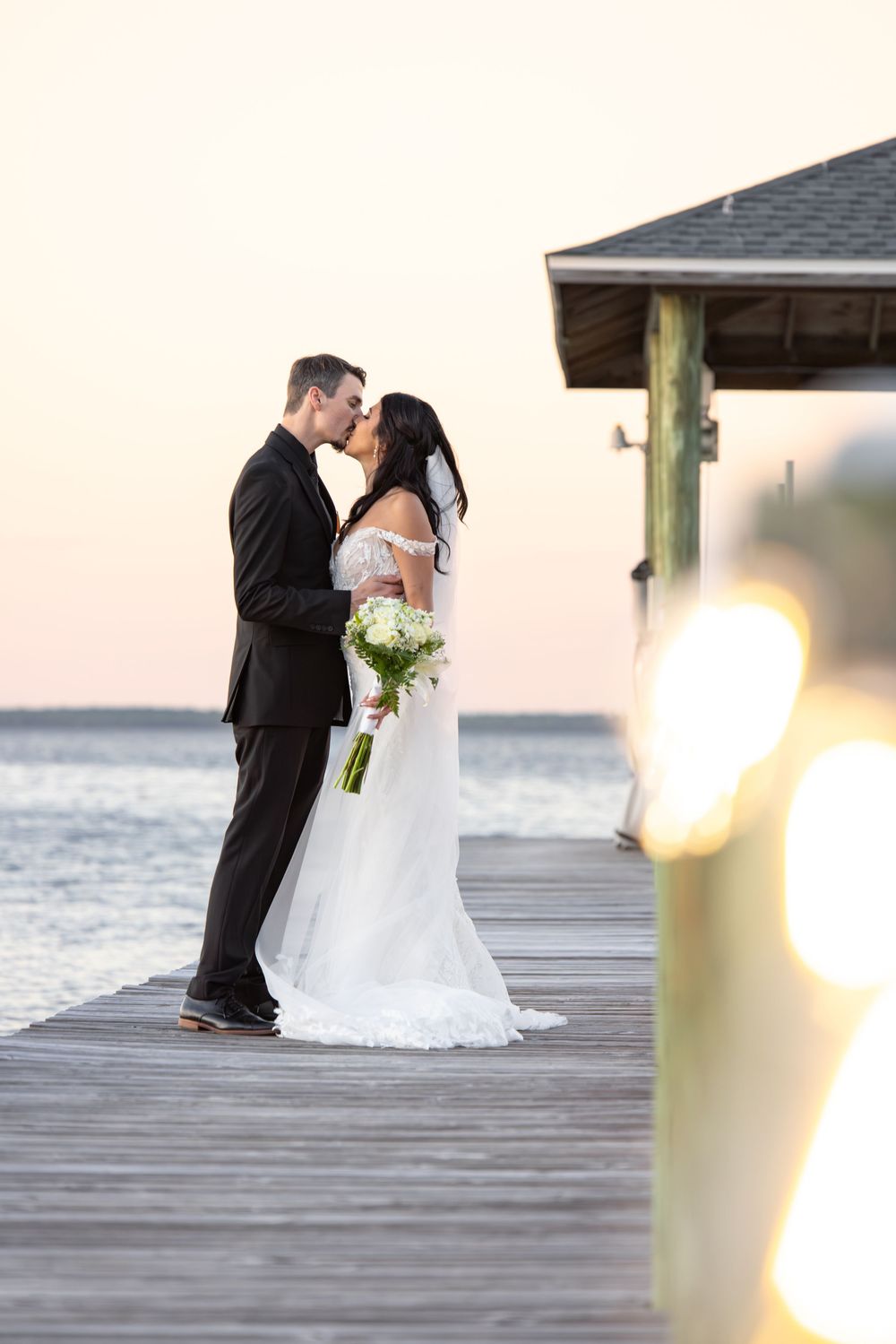 Romantic wedding couple embracing on wooden pier at sunset with ocean view.