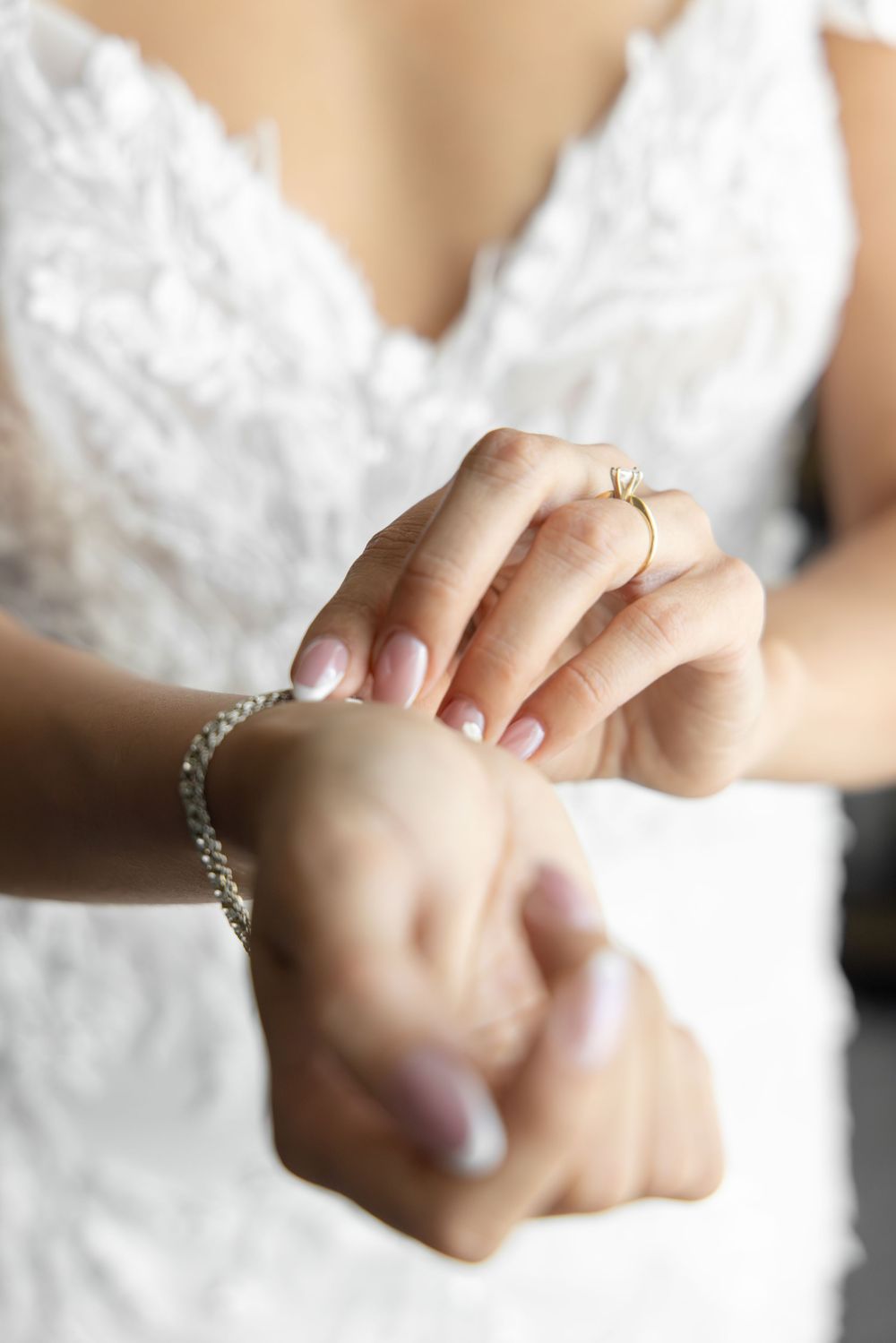 Close-up of delicate hands wearing a silver bracelet against white lace fabric.