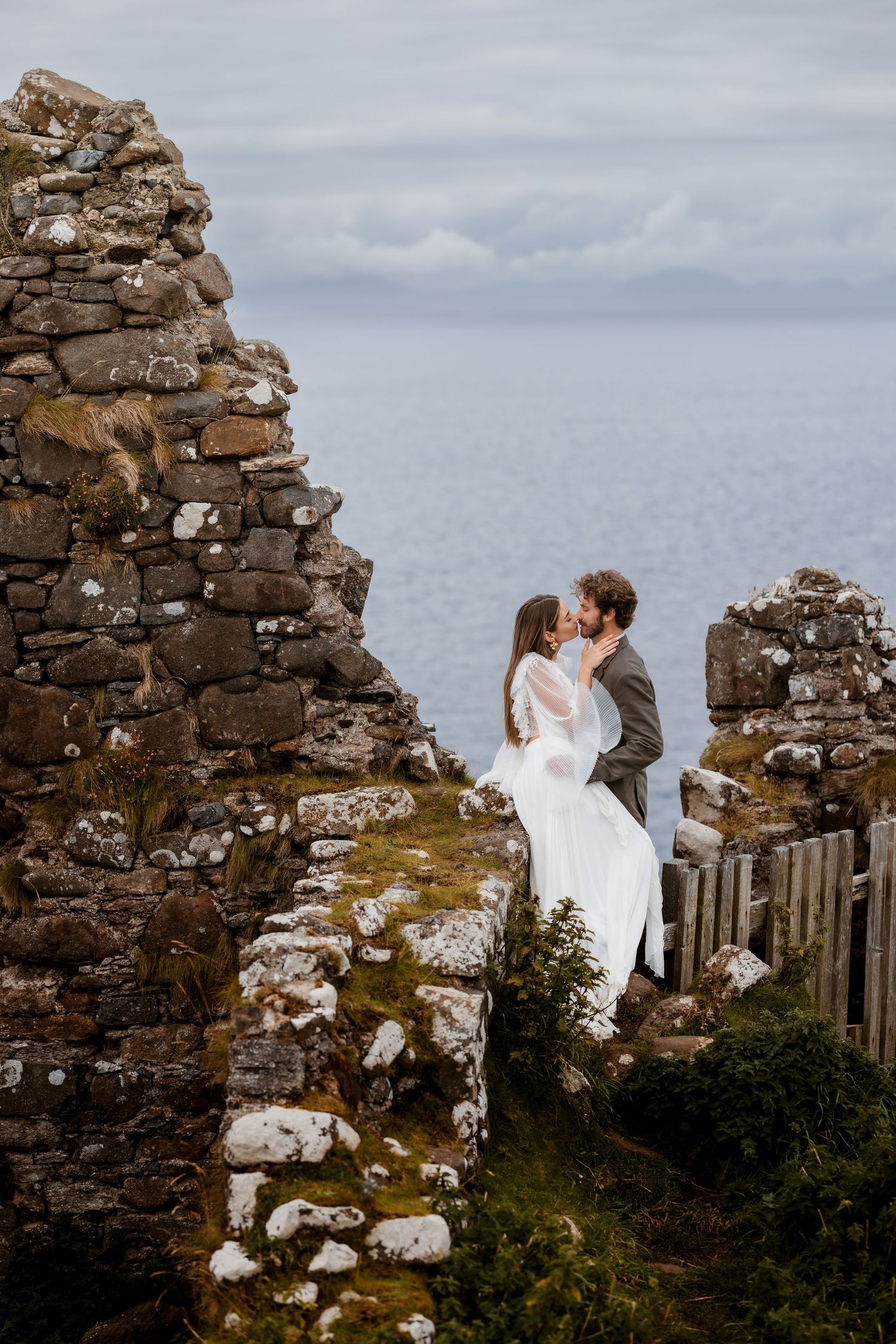 Ancient stone archway ruins overlooking a misty coastline with crumbling walls against a gray ocean backdrop.