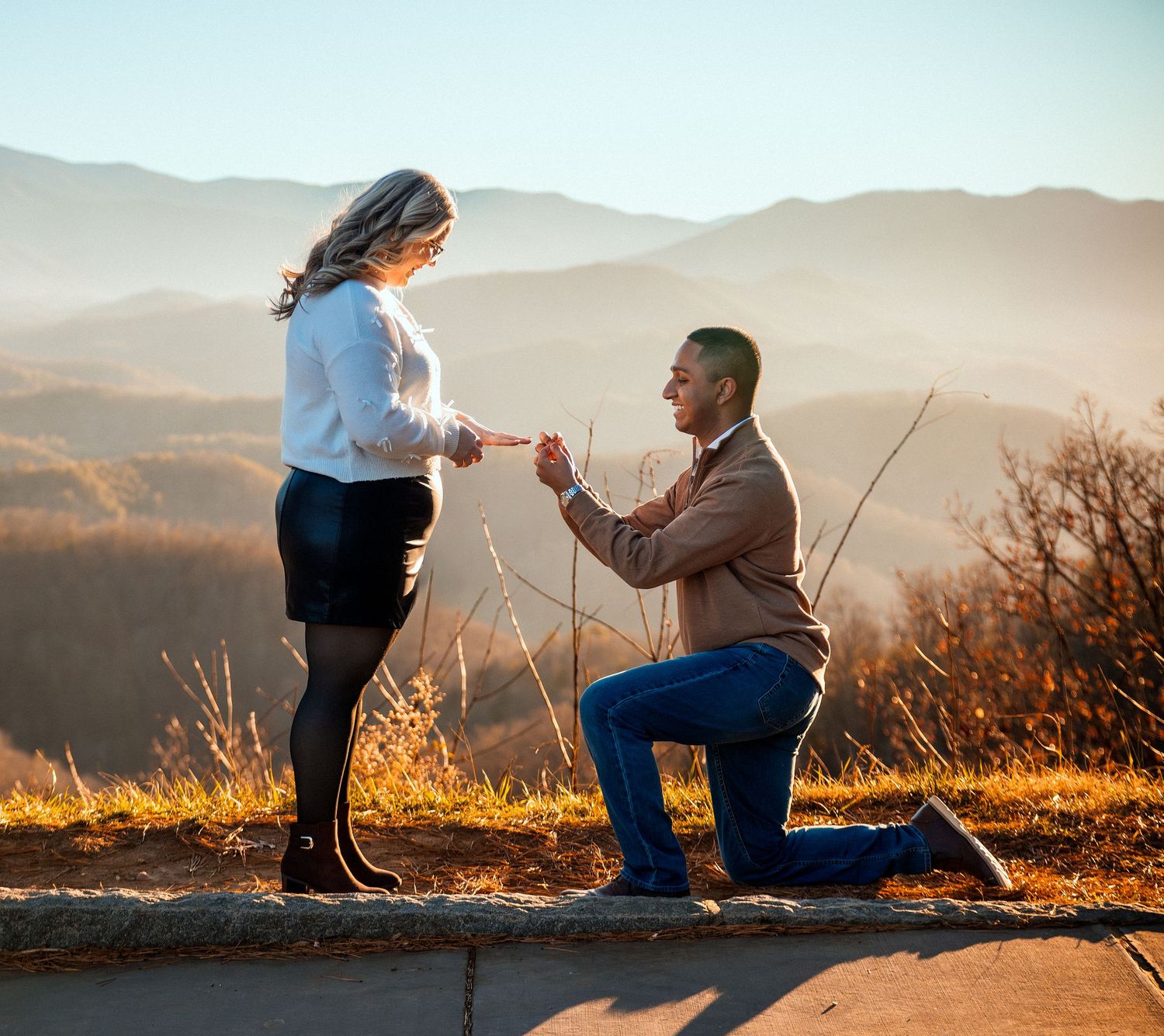 A romantic proposal takes place on a scenic mountain overlook at sunset with golden light illuminating the scene.