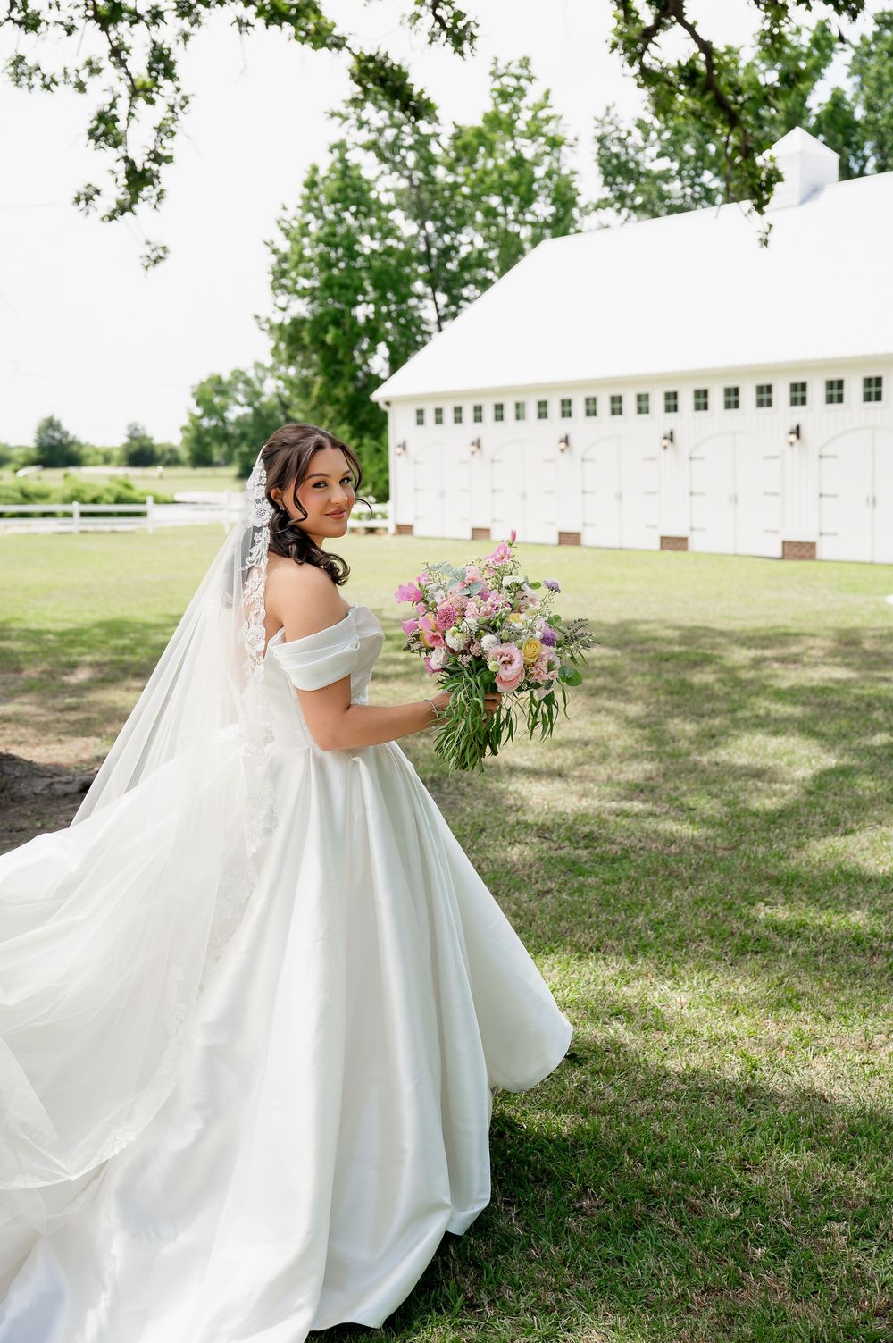 A flowing white wedding dress with a full skirt twirls against a grassy outdoor backdrop.