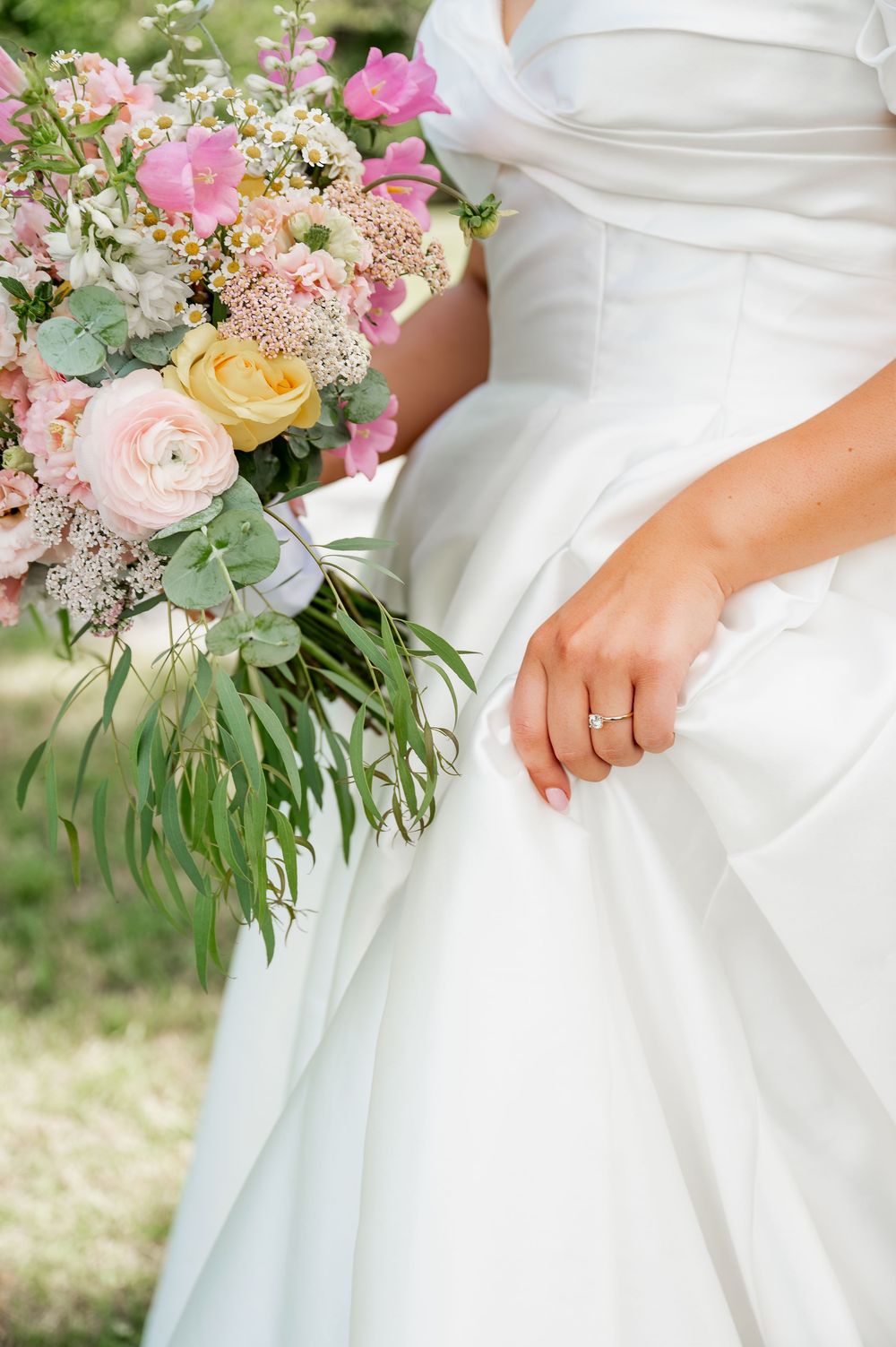 Close-up of pastel wedding bouquet with roses and greenery against white dress.