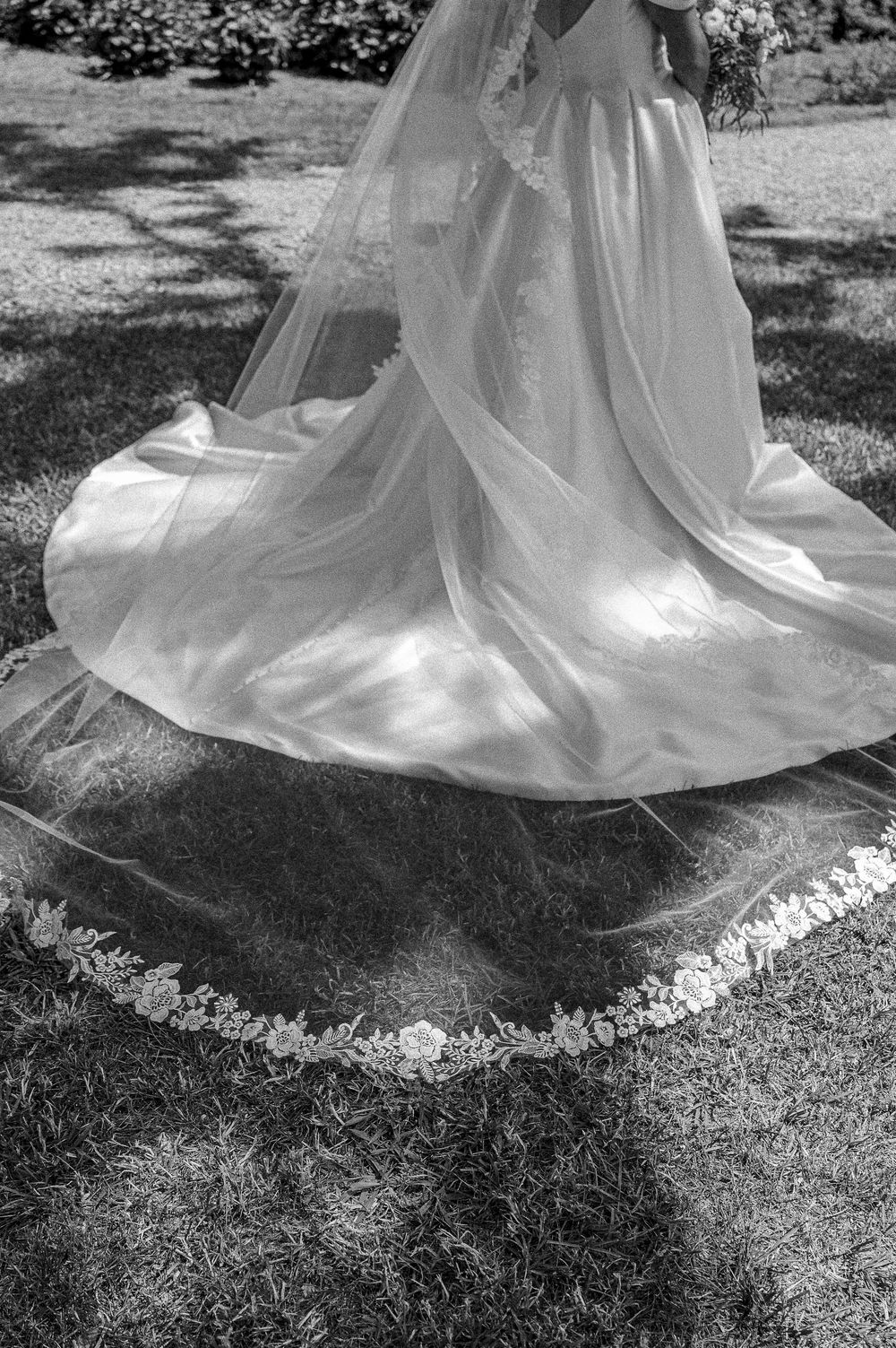 Black and white detail shot of an elegant wedding dress train on grass.