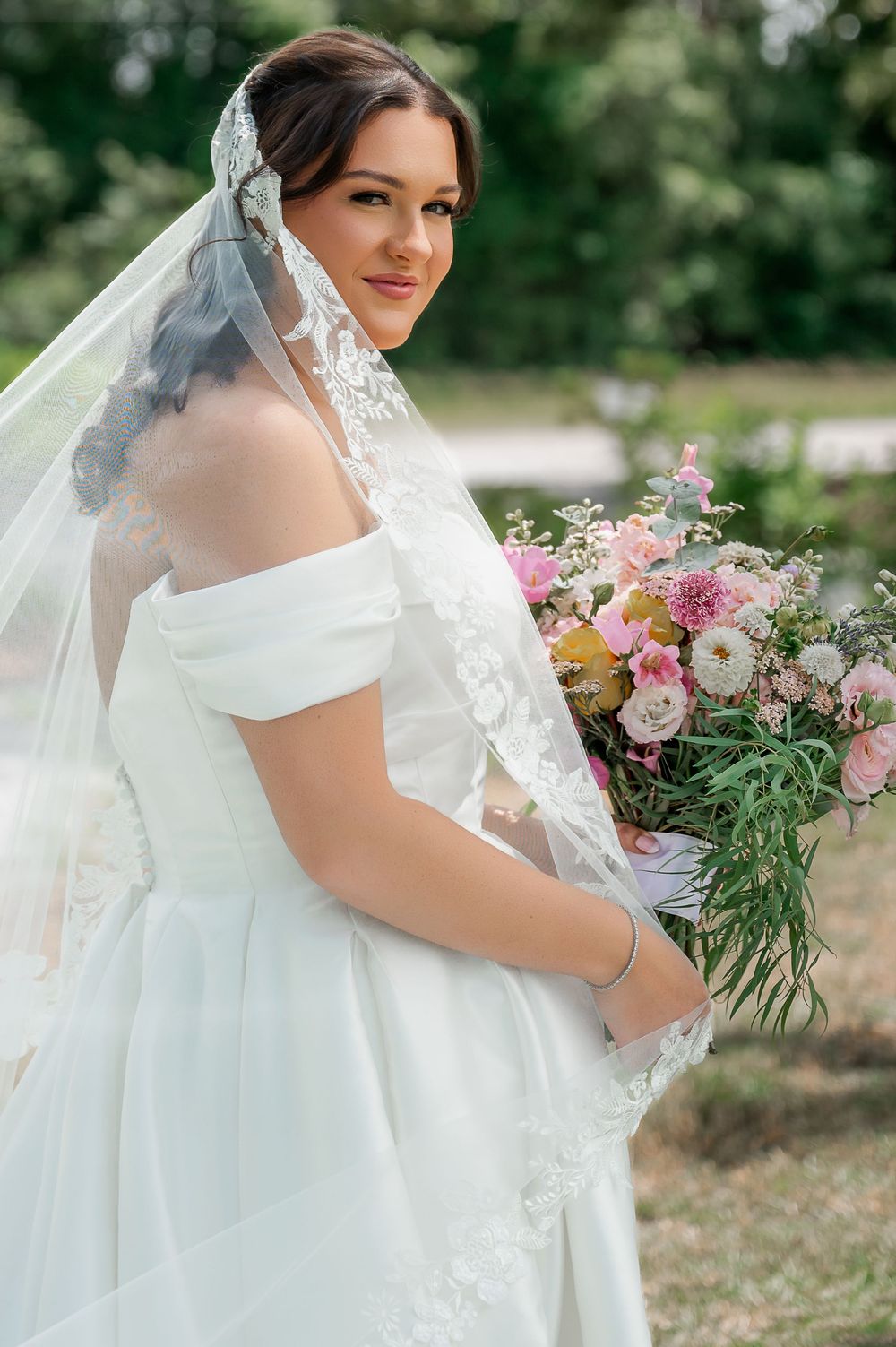 A classic white bridal gown with off-shoulder neckline is paired with a delicate lace veil.