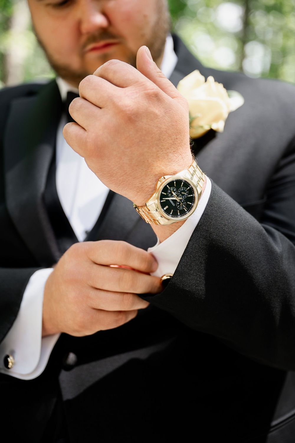 Close-up details of a gold watch and cufflinks on formal black suit attire.
