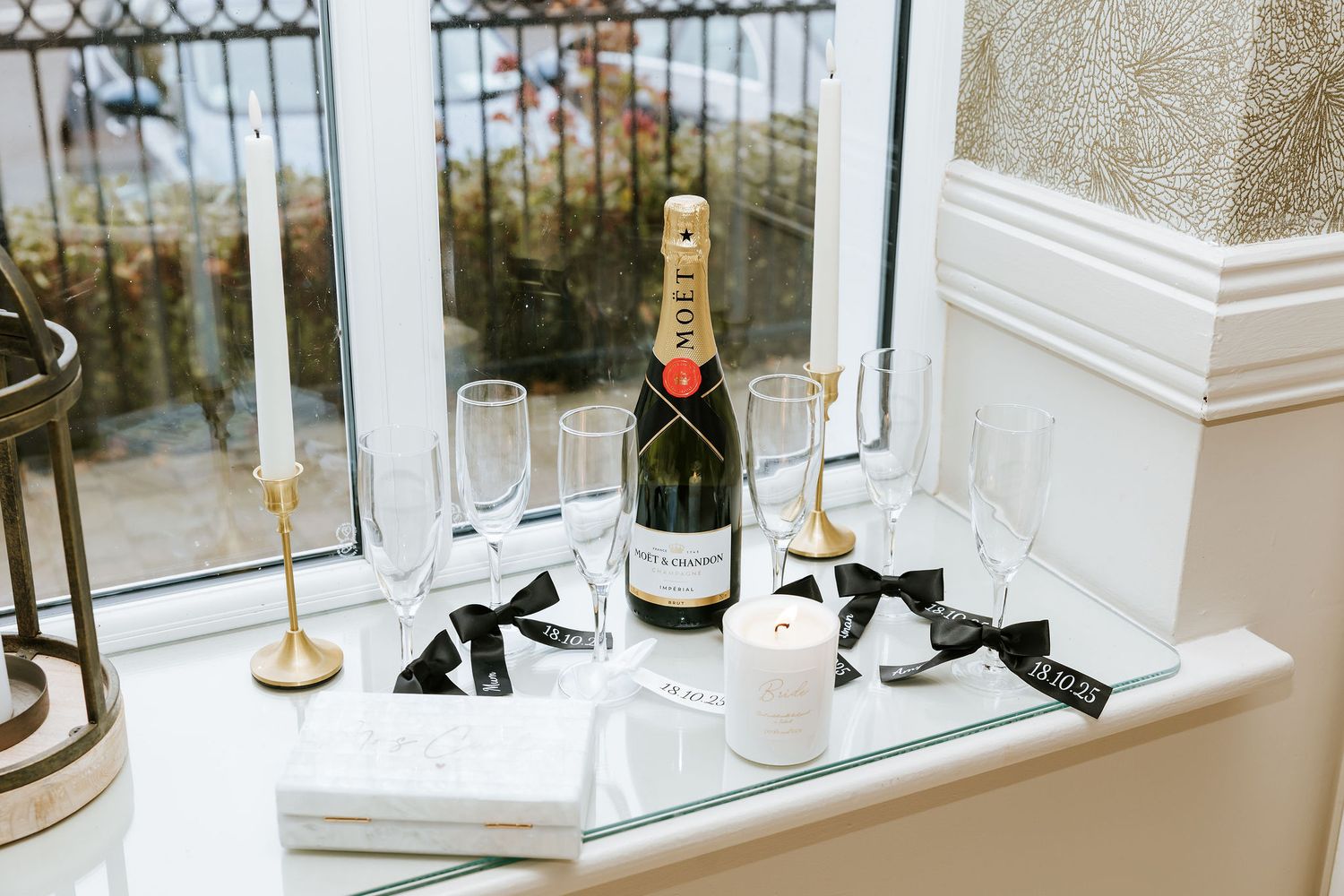 Elegant champagne glasses and bottle arranged on a white marble windowsill with city views in the background.