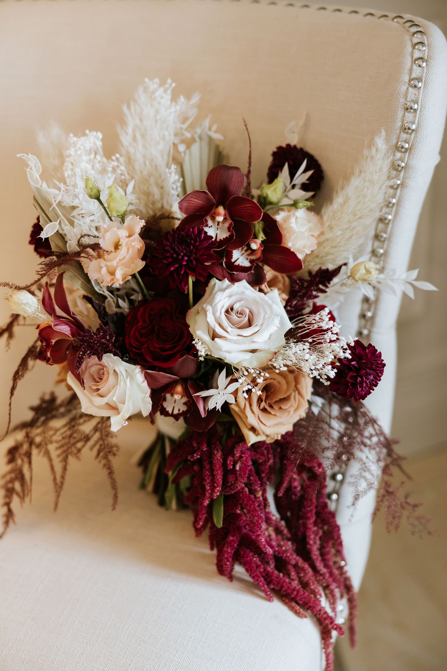 Wedding bouquet featuring burgundy amaranth, blush roses, and white flowers arranged in an elegant cascading style.