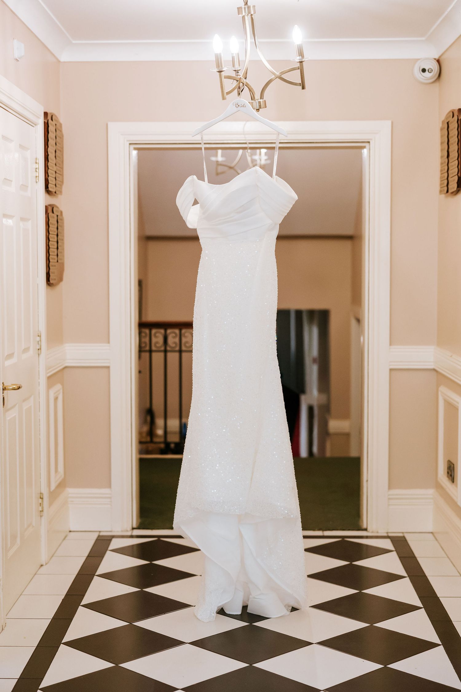 White wedding dresses hanging in an elegant hallway with black and white checkered marble flooring.