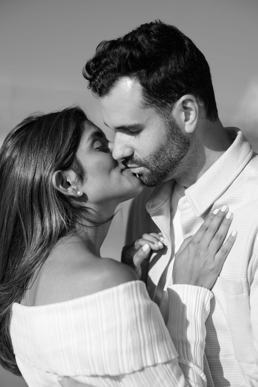 Black and white close-up of a couple about to kiss, woman in white off-shoulder top touching mans chest.