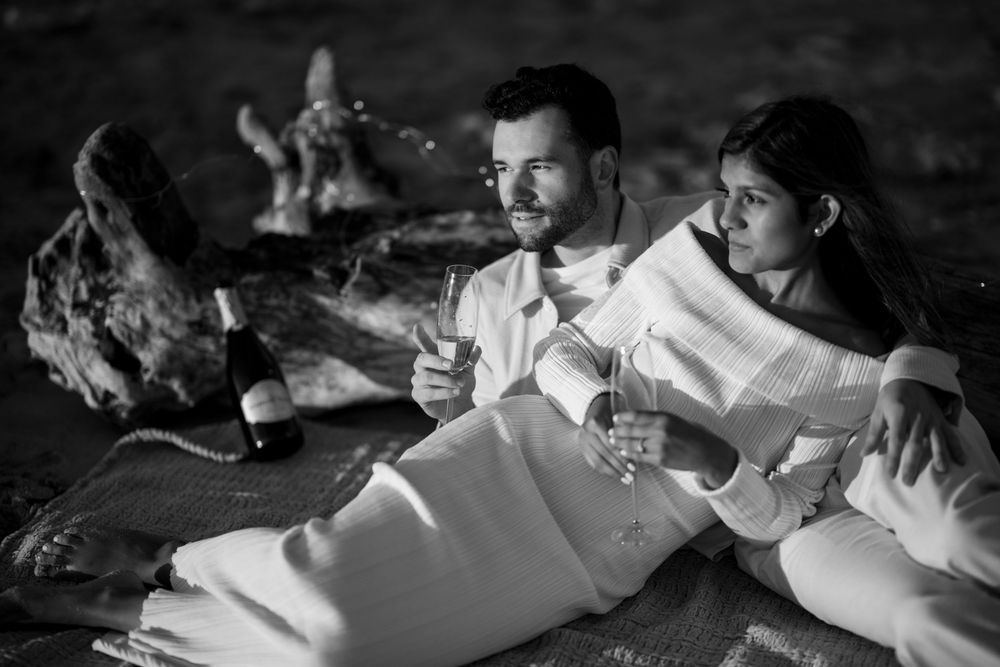 Black and white photo of a couple relaxing on a blanket sharing champagne at night.