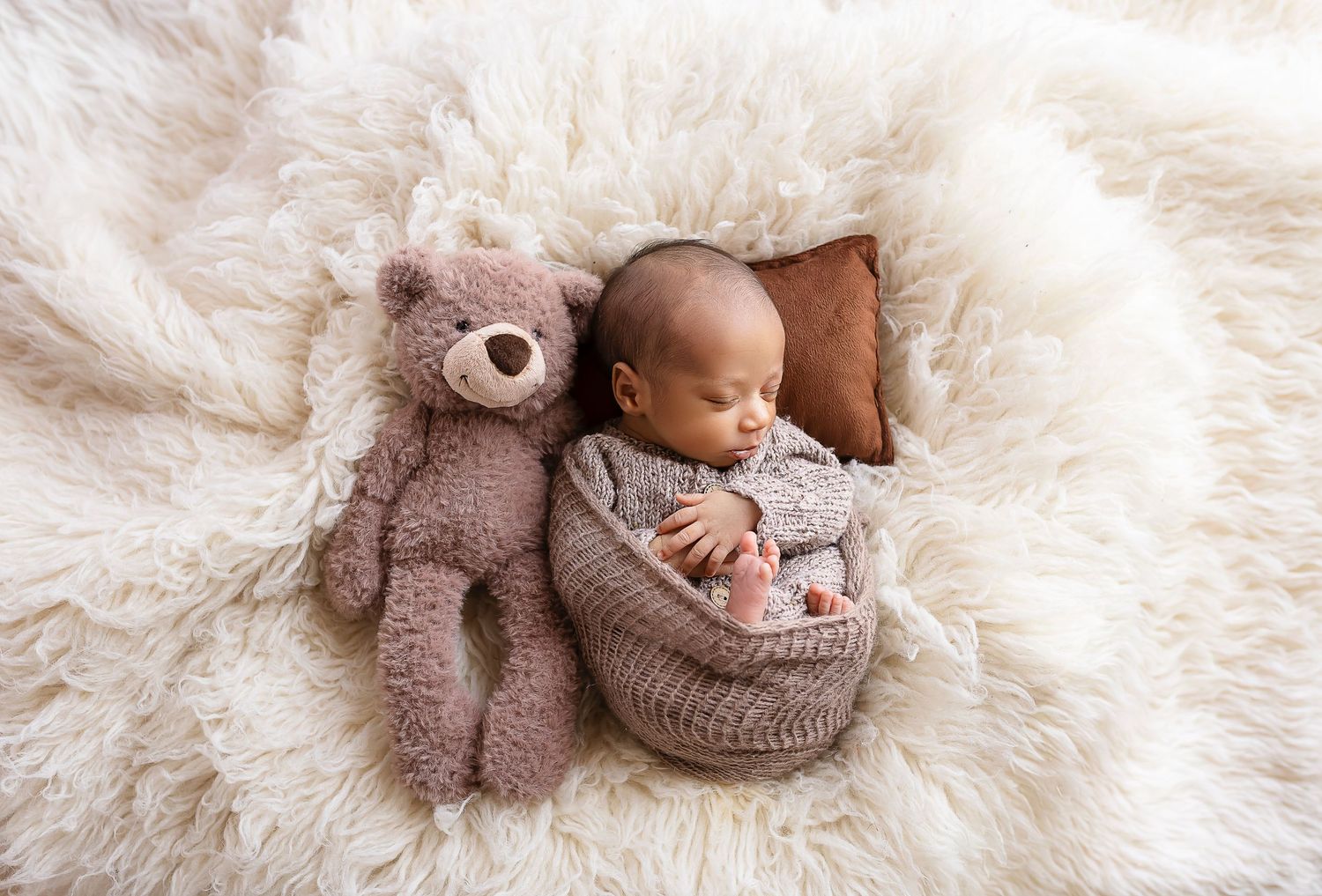 bebe envuelto en manta tejida color marron junto a un osito, elementos cremas y marron fotografa de bebes