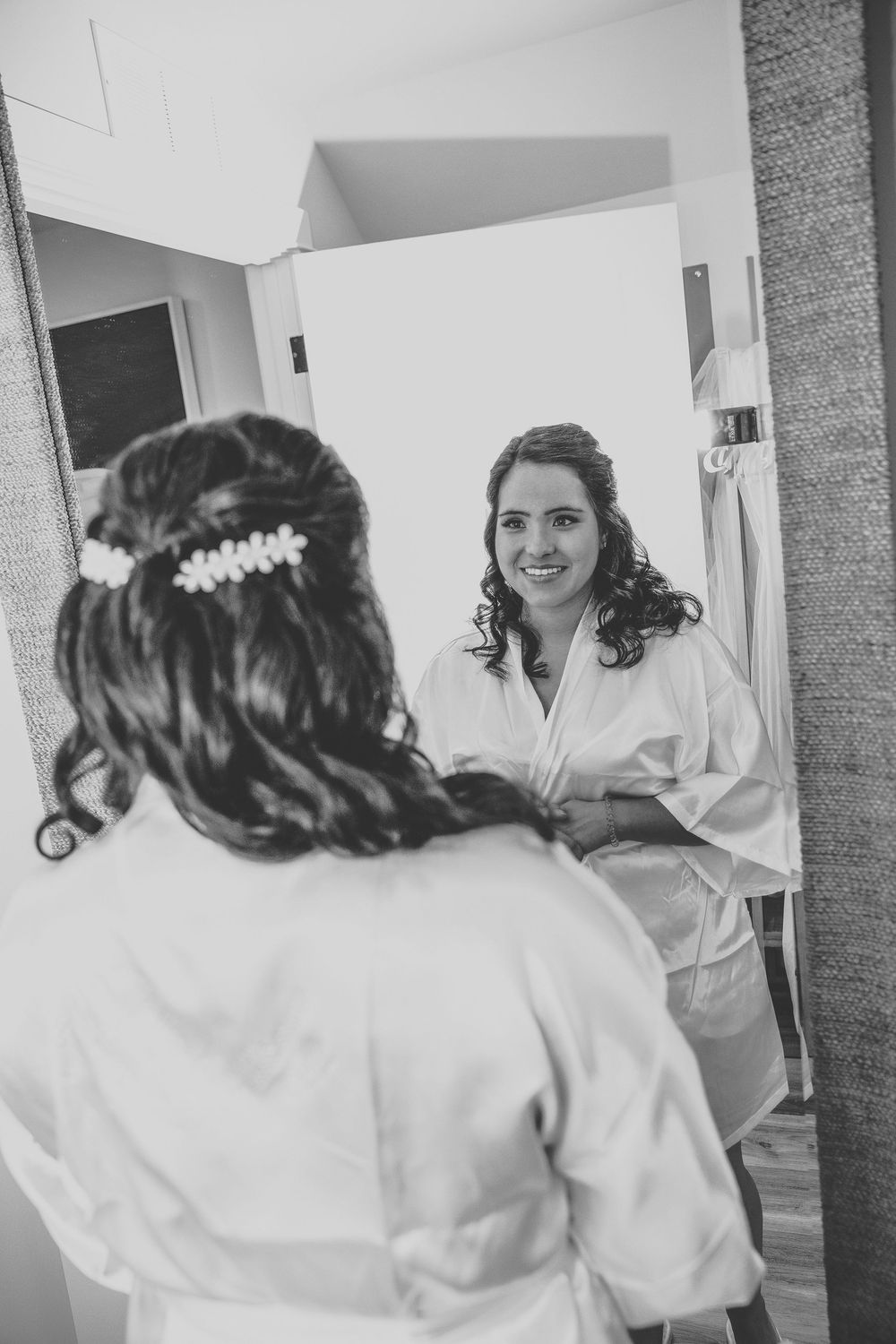 A black and white mirror reflection of a bride in her robe applying makeup.