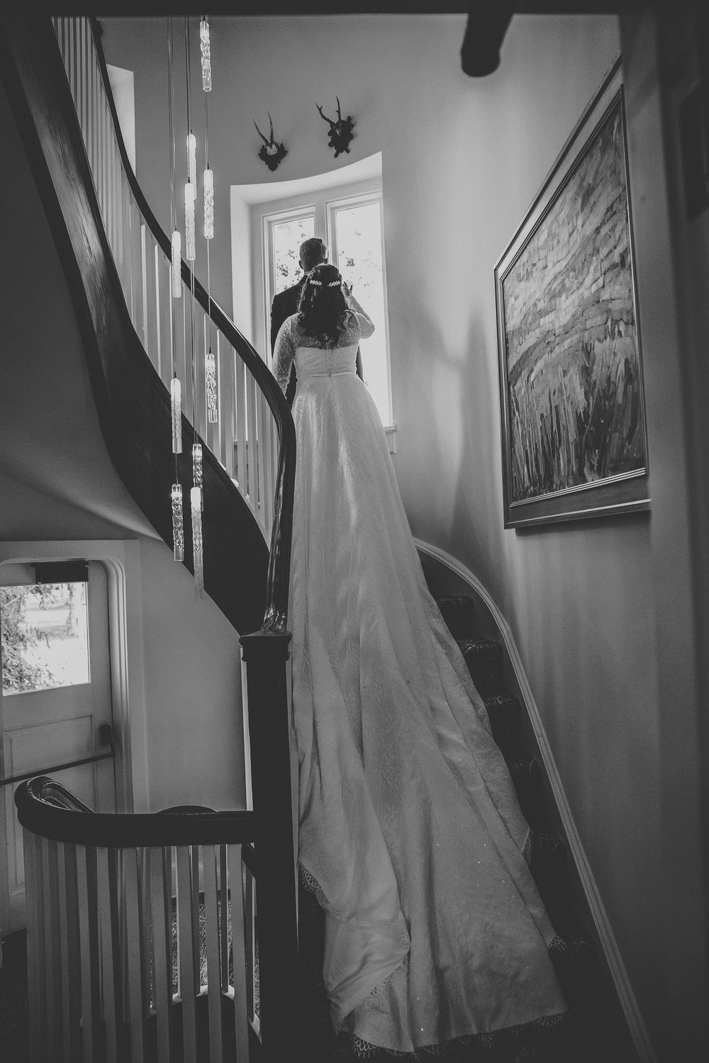 A bride elegantly on a staircase with mounted deer heads and framed artwork visible in the background at their first look