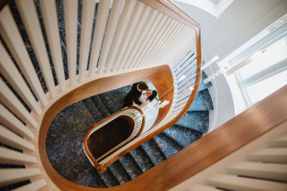 Looking up a curved wooden staircase with white spindles and dark carpet runner spiraling towards natural light from above.