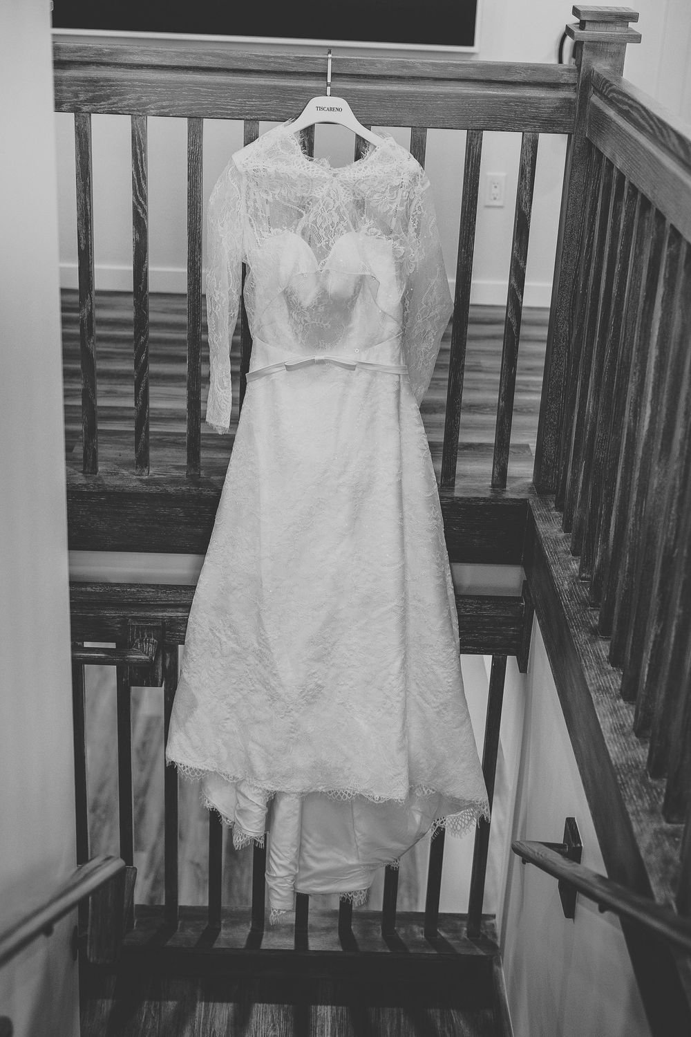 A black and white photo of a lace wedding dress hanging from a staircase.