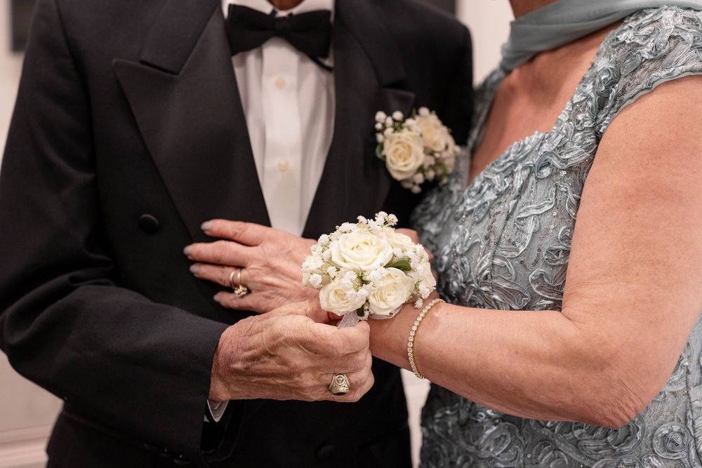 A formal wedding party poses together in black suits and elegant dresses with white floral bouquets.