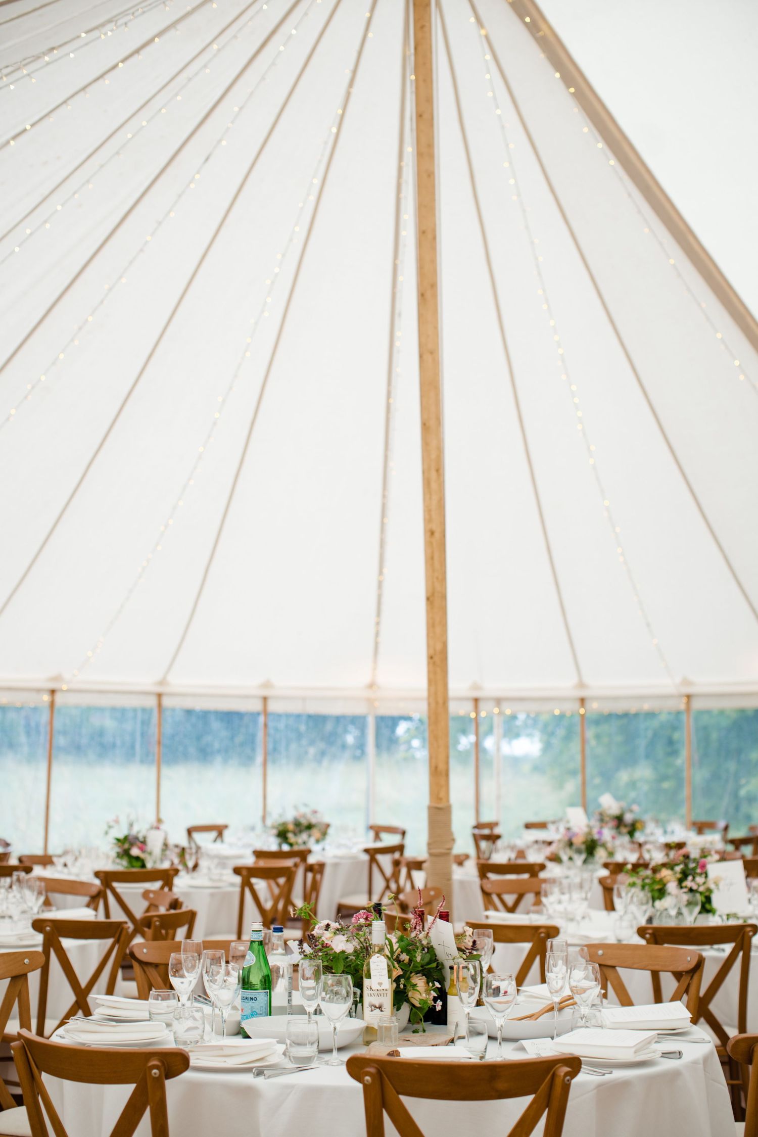 Elegant wedding reception tables set under a white tent canopy overlooking a waterfront view.