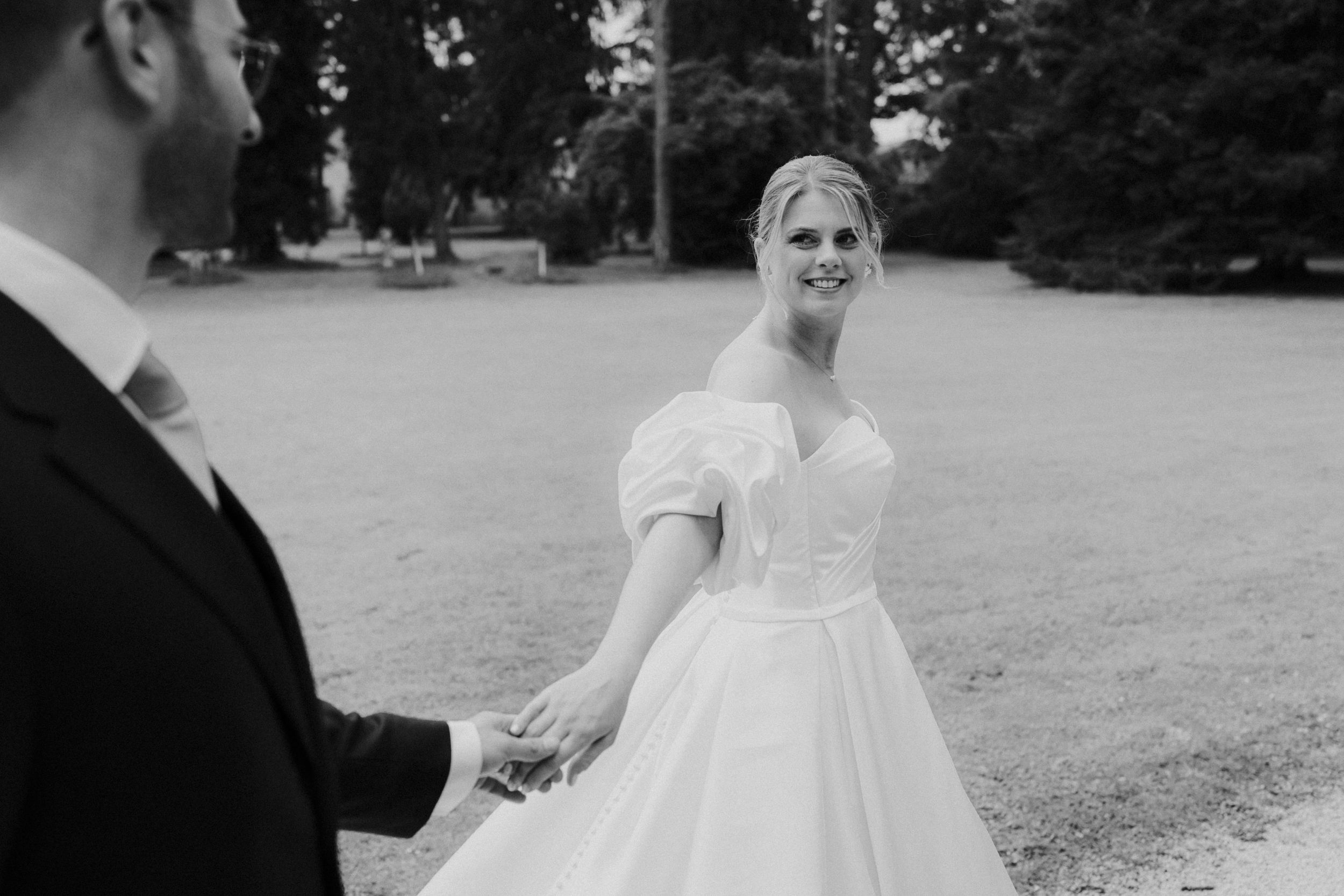 A bride in a white ballgown wedding dress smiles during a black and white outdoor wedding moment.