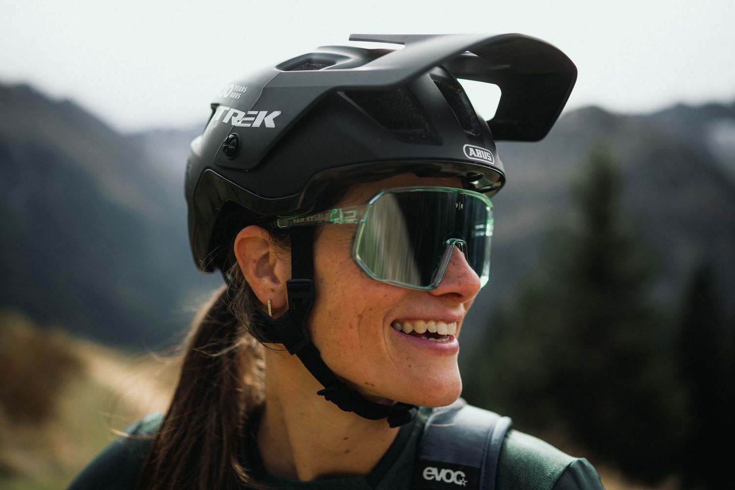 Mountain biker wearing a black helmet and reflective sunglasses smiles while enjoying an outdoor adventure.