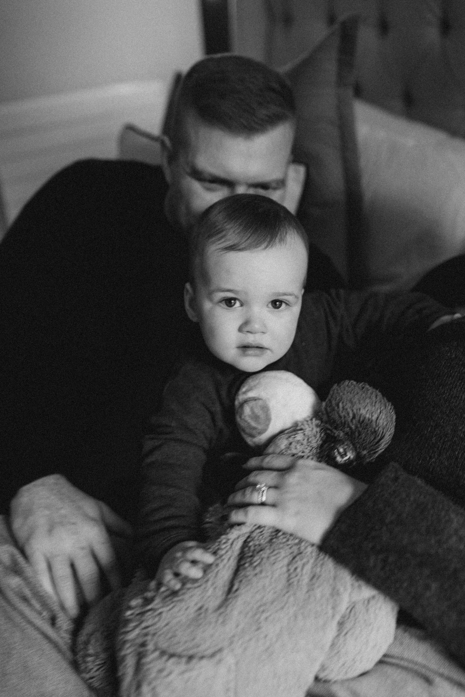 a baby boy looking into the camera while his father kisses the back of his head lovingly