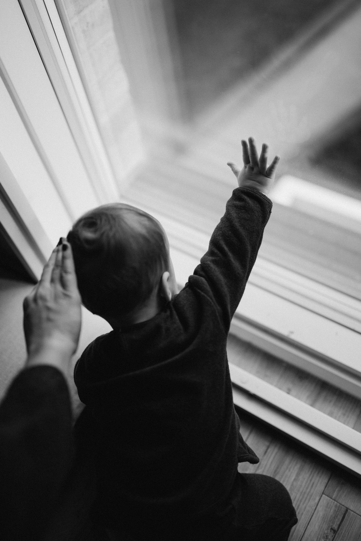 a baby touching the window while his mother is touching his head