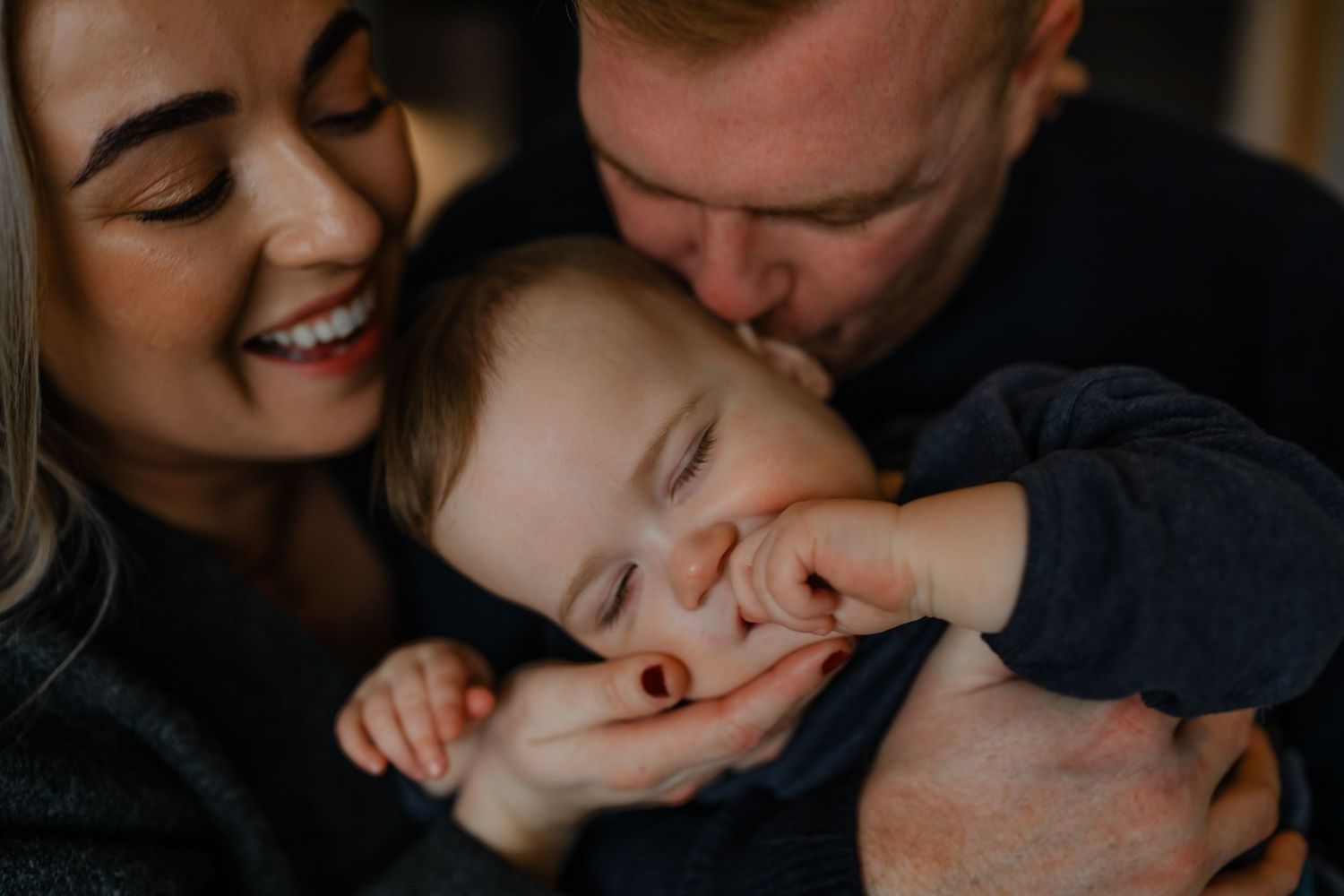 a close up of two parents holding their baby son close to their faces