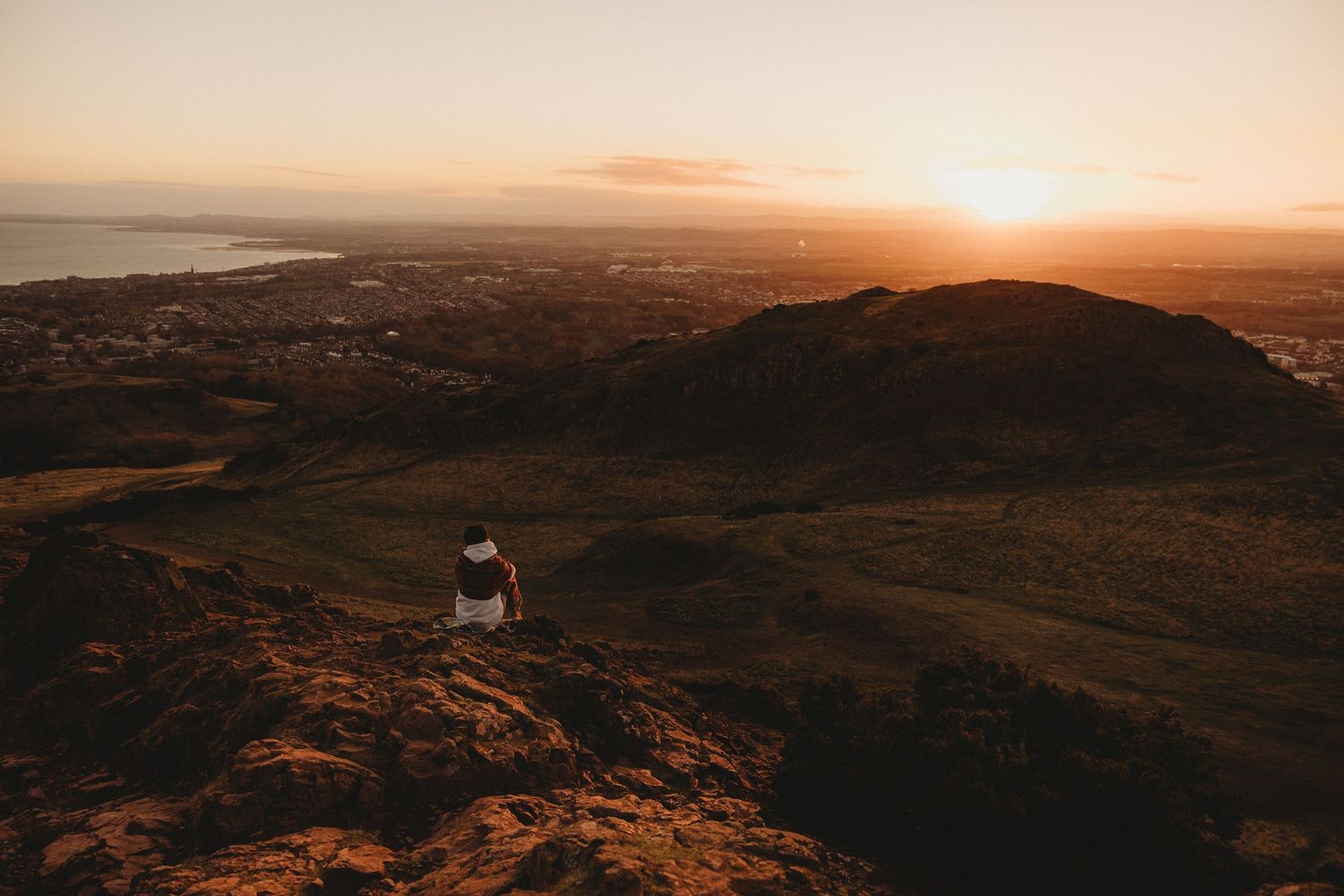 Panoramic mountain landscape at golden hour with dramatic shadows cast across rolling hills and valleys at sunset.